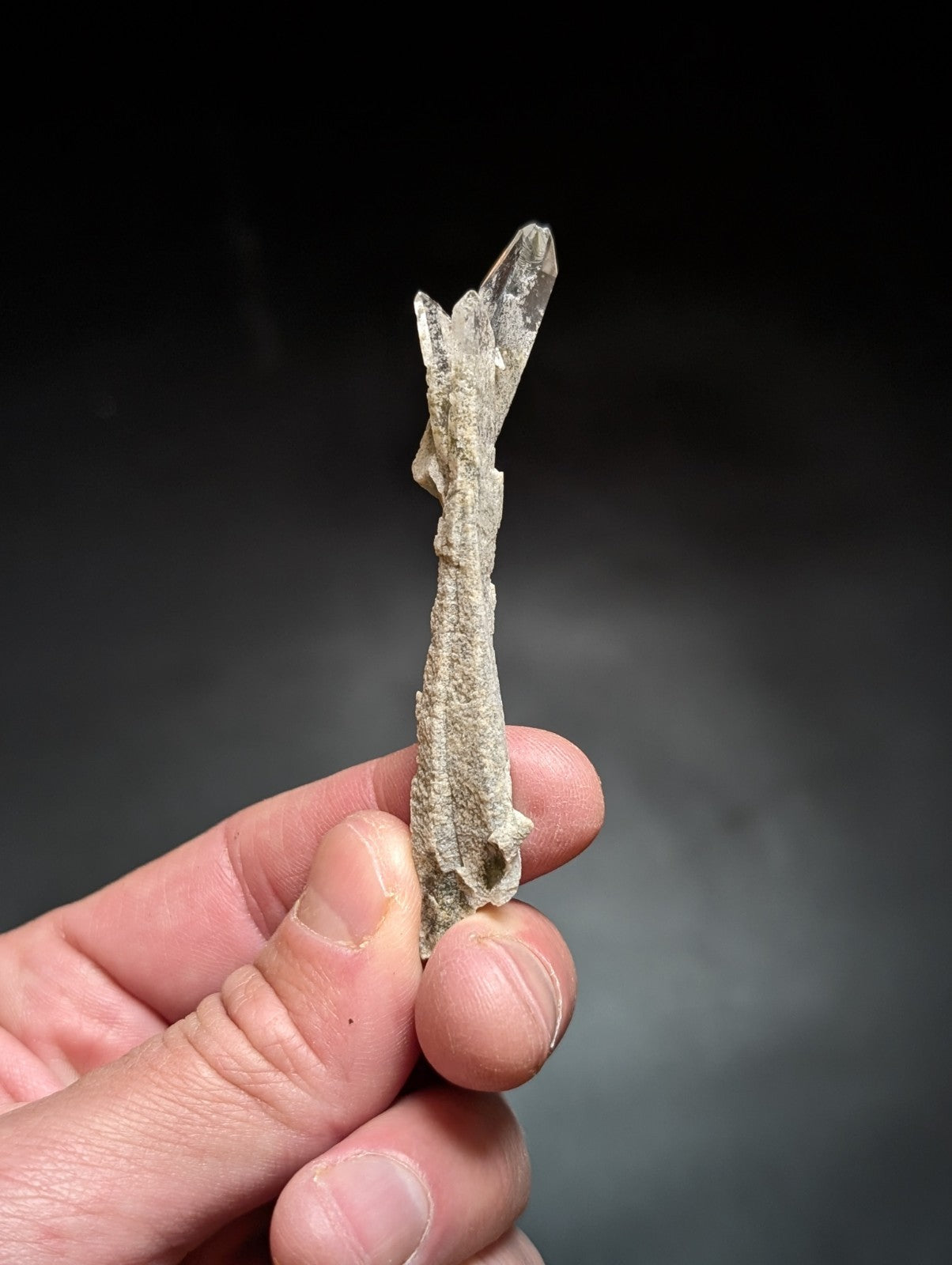 A translucent, clear quartz crystal cluster with a rough, earthy base and sharp, pointed terminations.