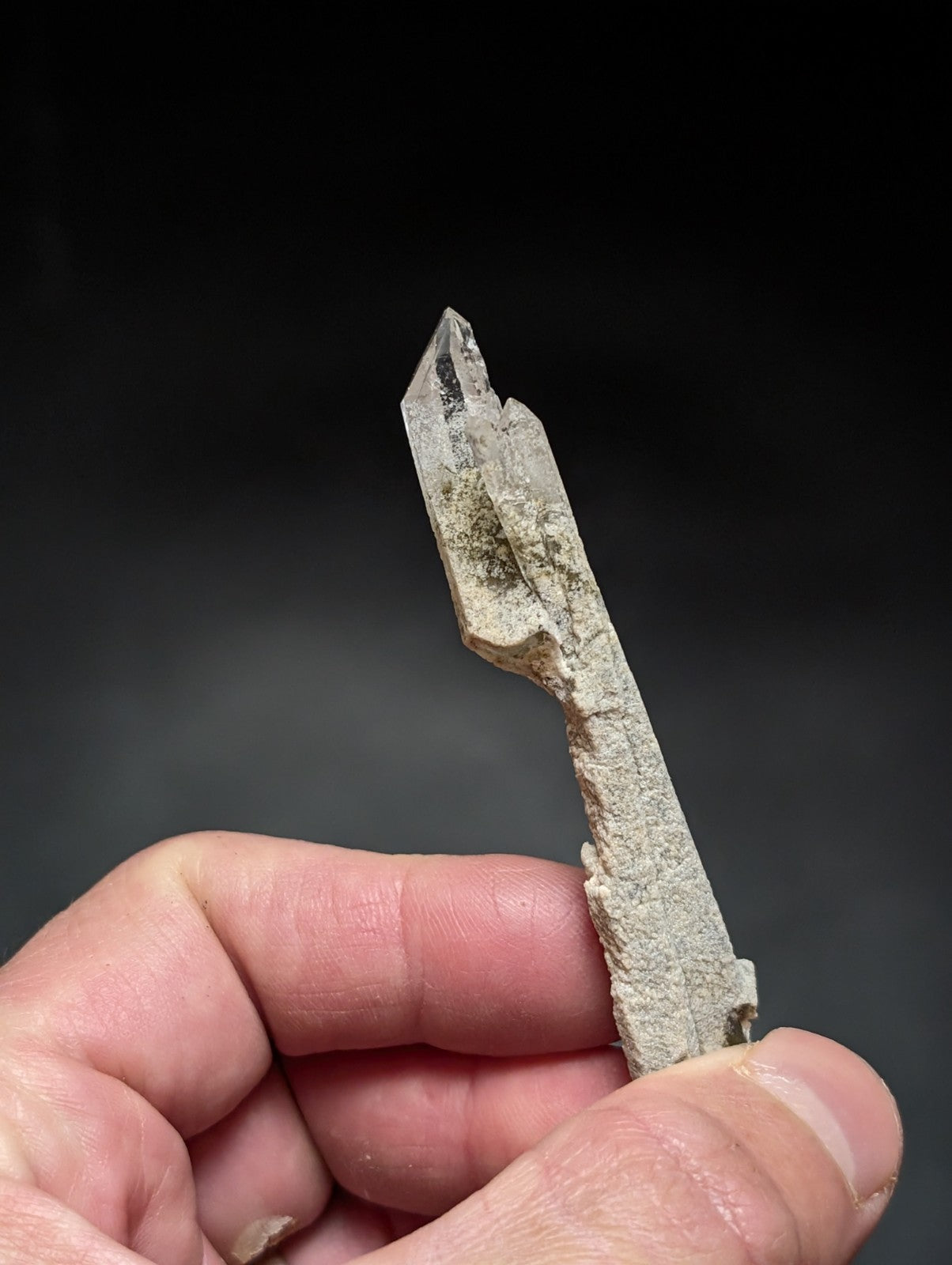 A translucent, pointed quartz crystal with a rough, earthy base and natural imperfections.