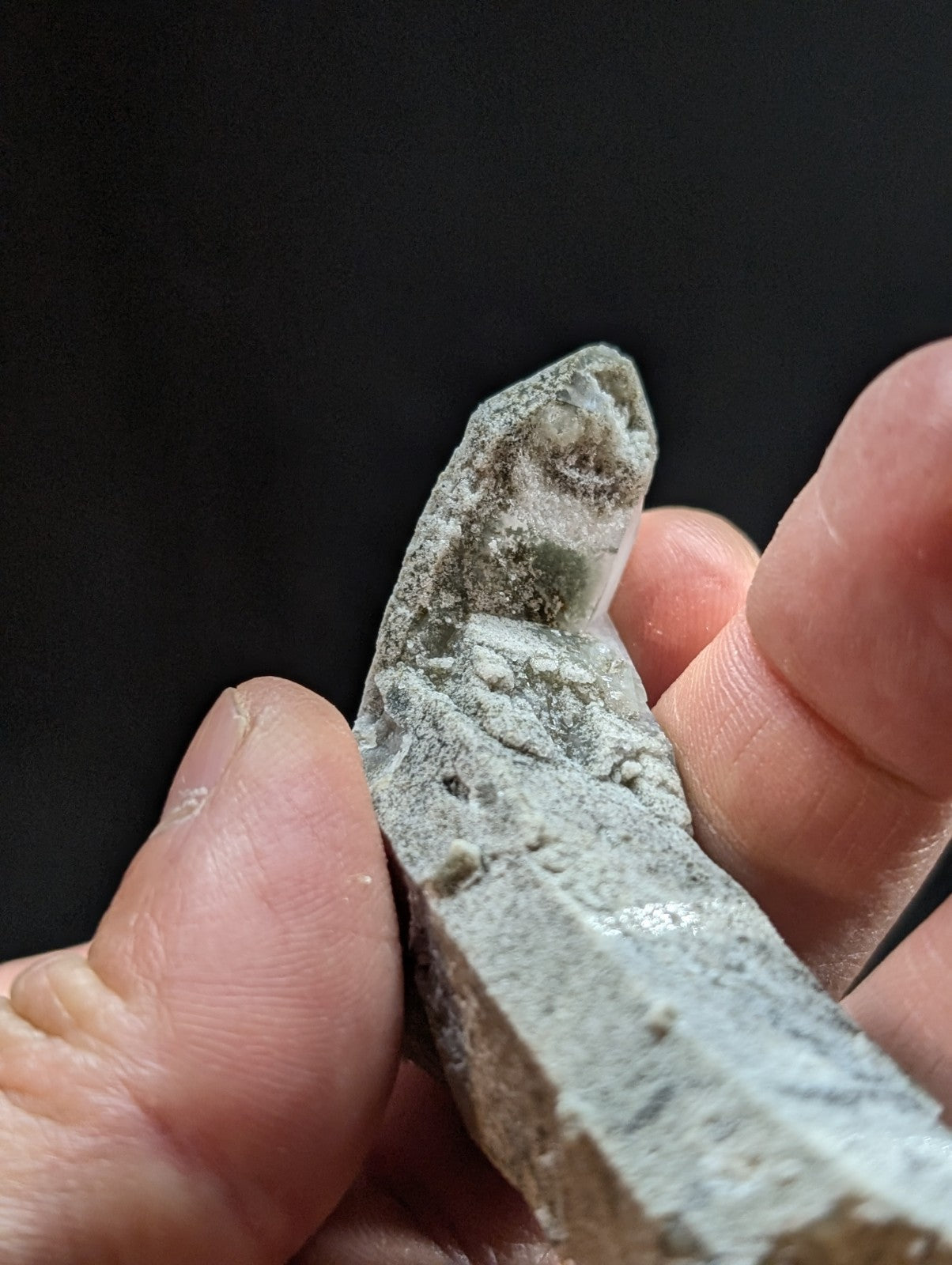 A weathered, grayish-green stone fragment with a carved face and textured surface.