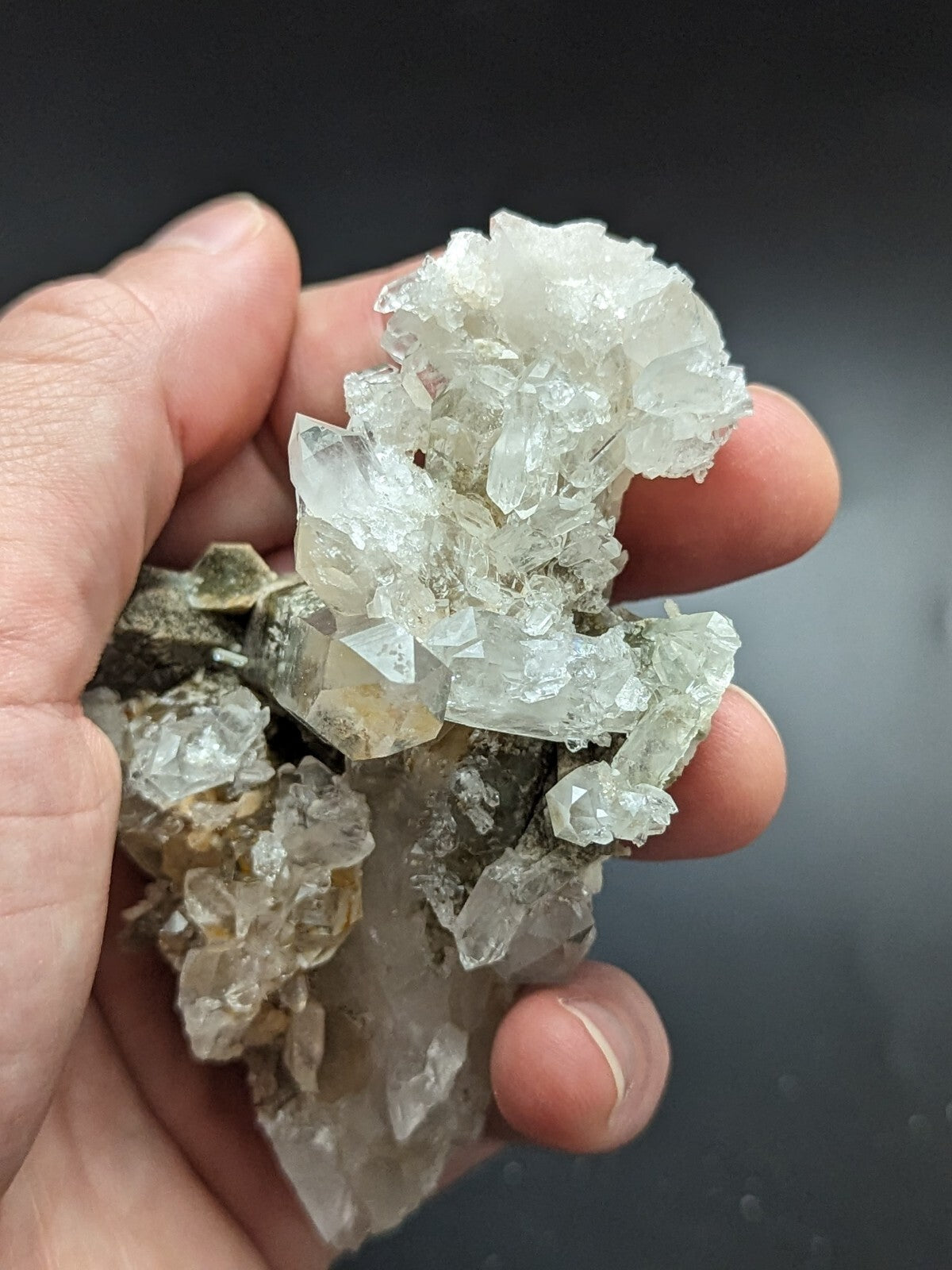 A hand holds a cluster of translucent, crystalline quartz formations with clear and pale greenish hues.