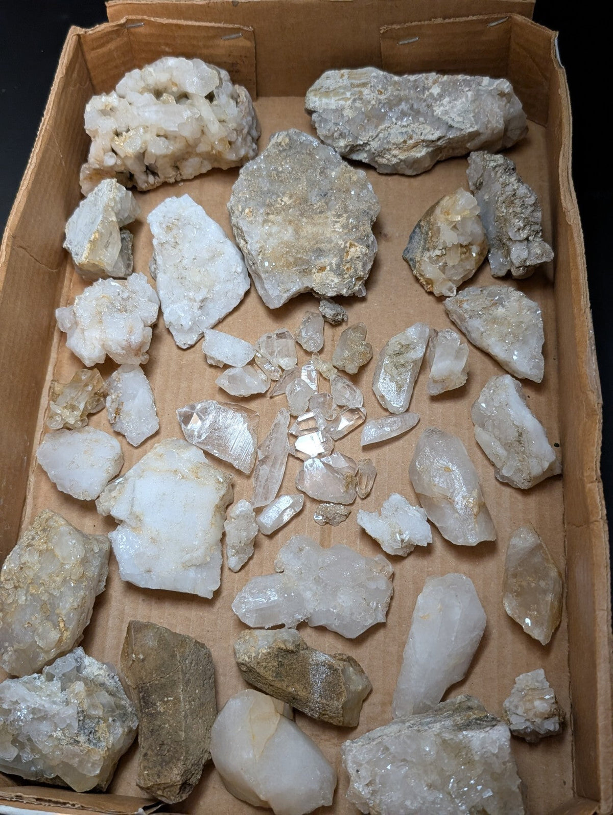 A collection of raw, translucent quartz crystals and mineral specimens in various sizes and shades of white, clear, and pale gray.