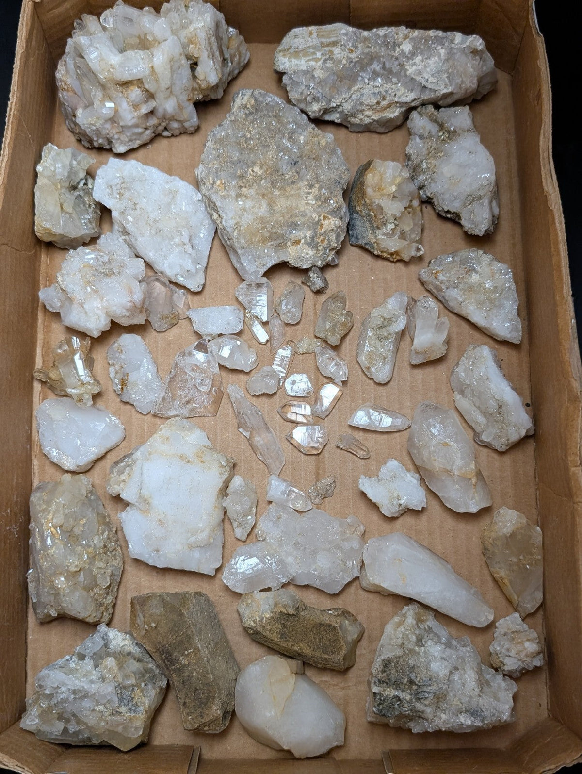A collection of raw, translucent quartz crystals in varying sizes and shapes with some exhibiting golden flecks.