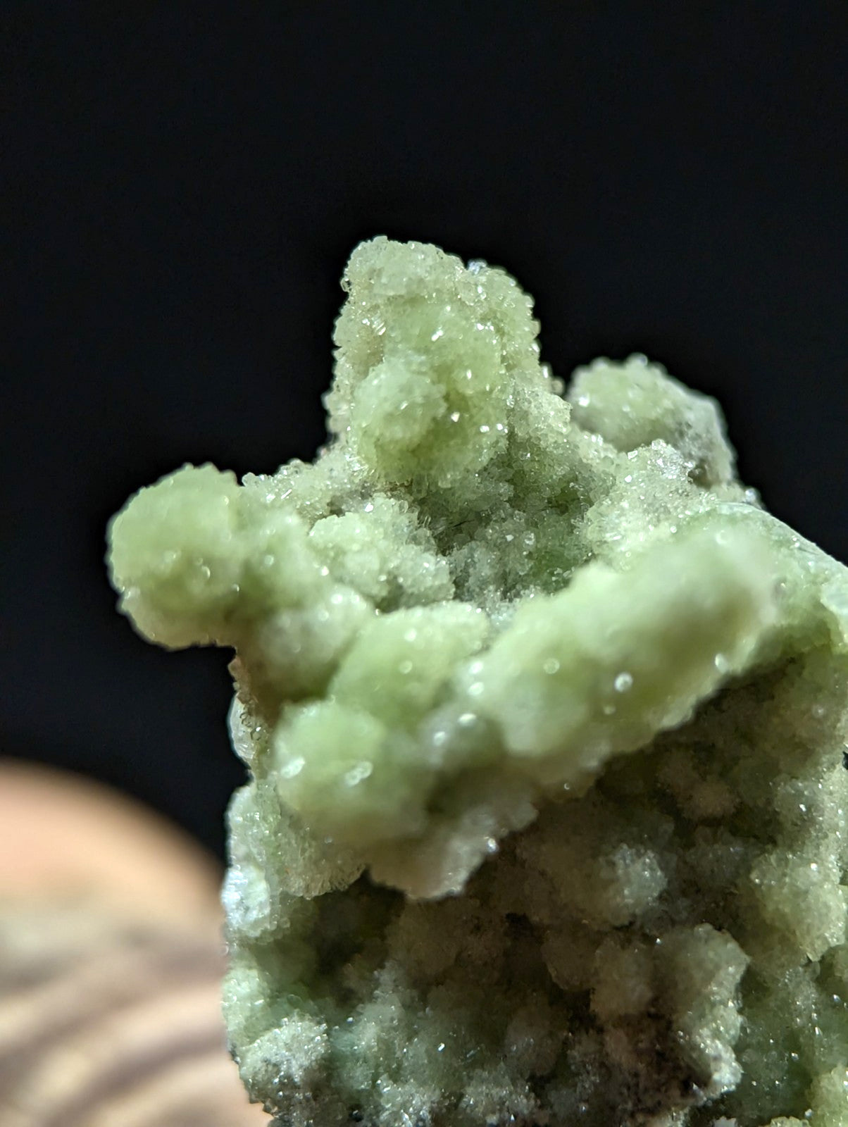 A pale green, crystalline mineral specimen with a rough, textured surface and translucent facets.