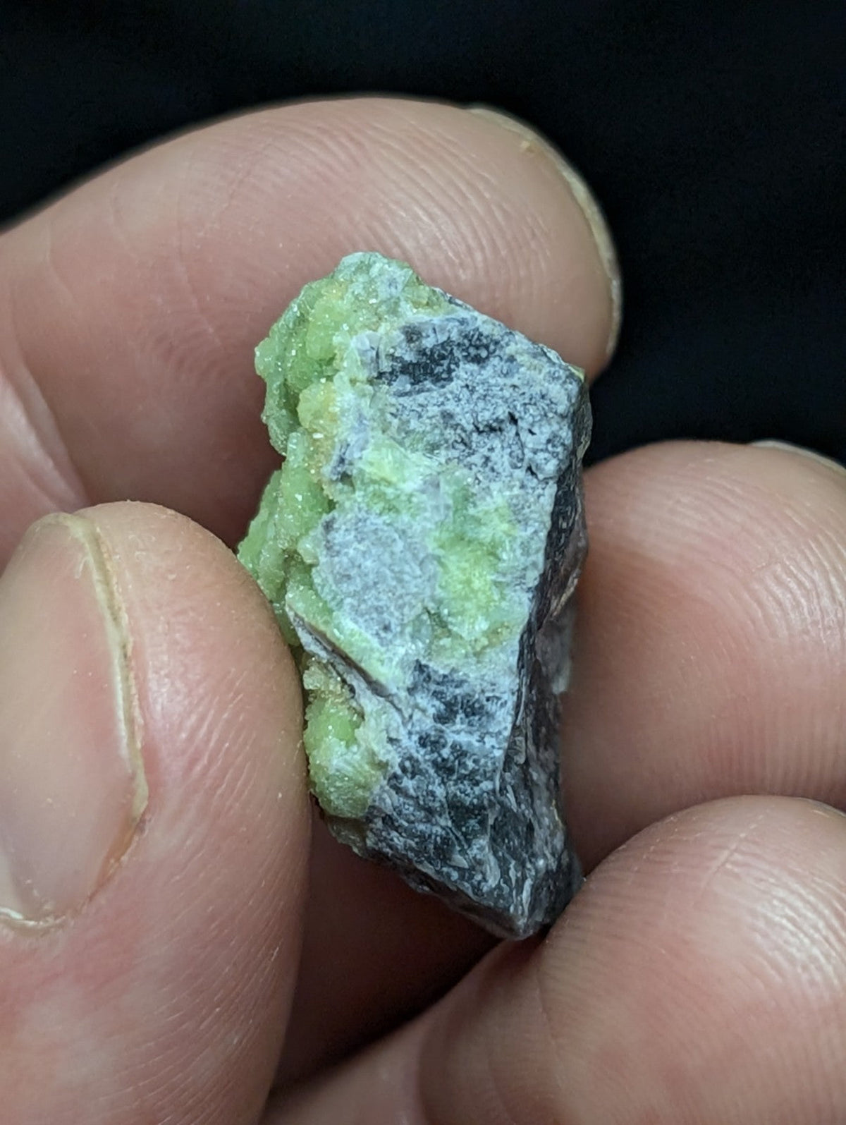 A rough, irregularly shaped mineral specimen with a vibrant green crystalline formation contrasting against a darker gray matrix.
