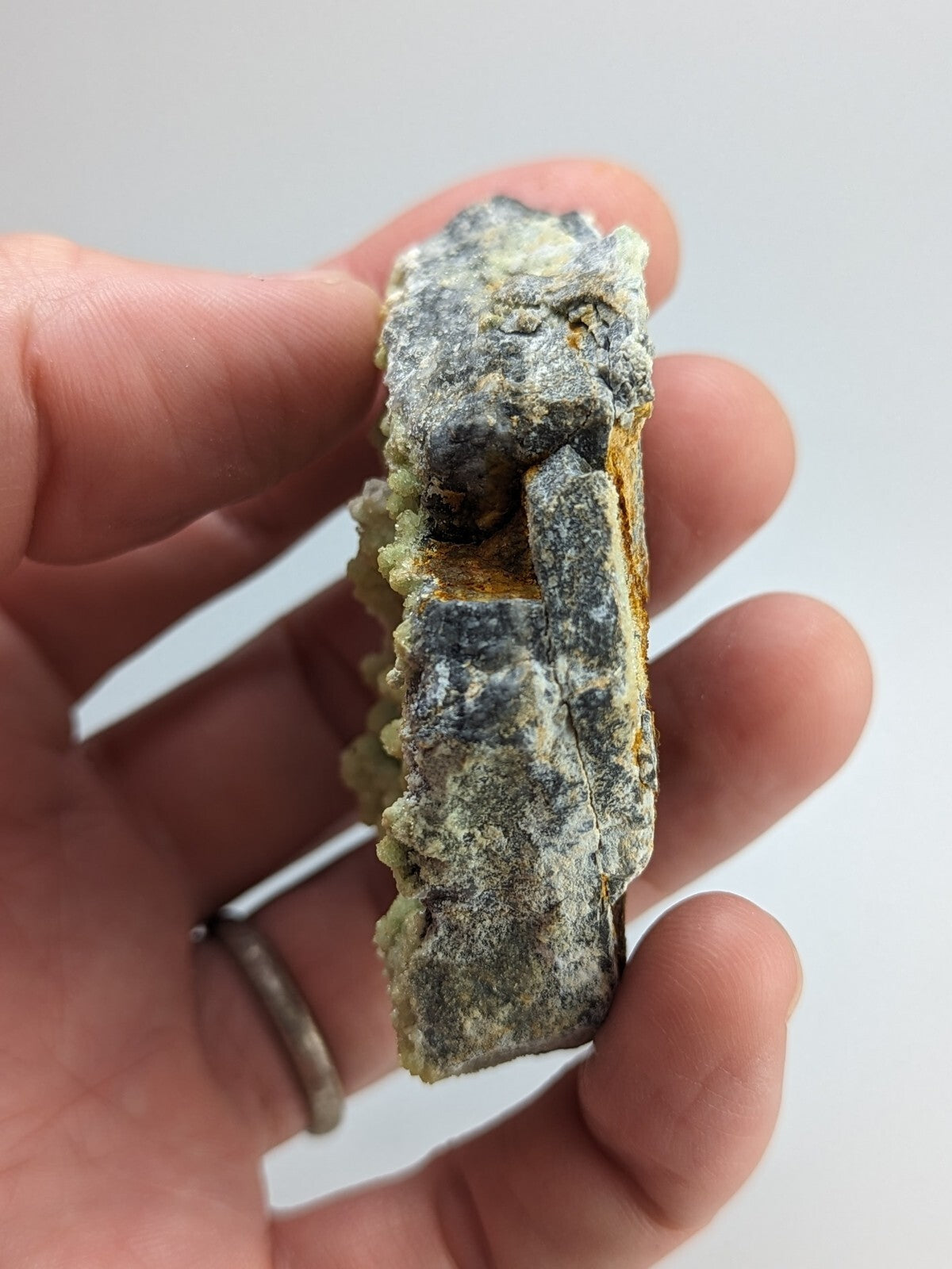 A rough, irregularly shaped mineral specimen with a grayish-green surface and patches of yellow-orange oxidation.