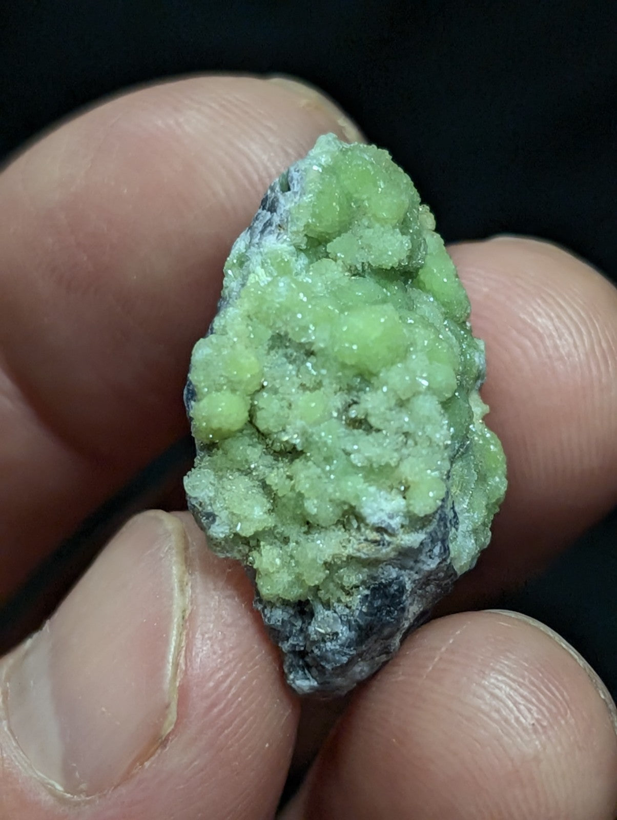 A vibrant green, crystalline mineral specimen with a rough, textured surface and dark gray matrix.
