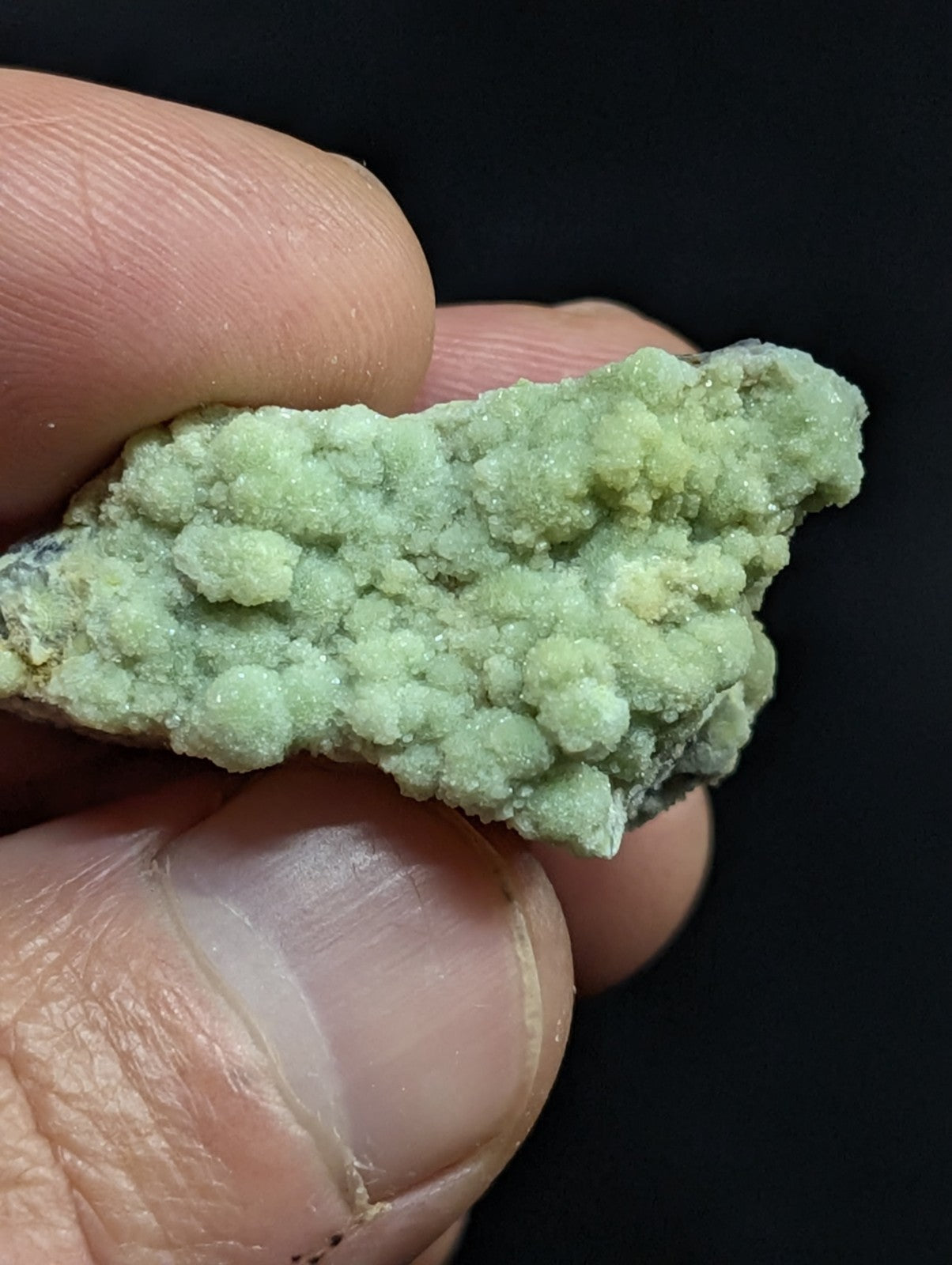 A pale green, textured mineral specimen with a crystalline surface held in fingers.