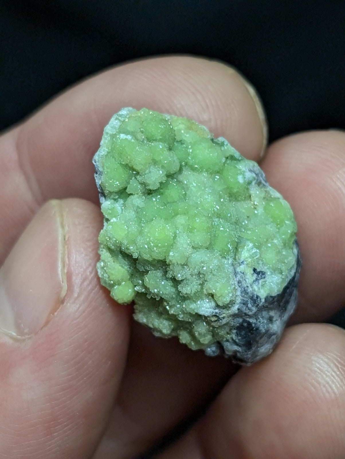 A vibrant green, crystalline mineral specimen with a rough, textured surface and some darker matrix material.