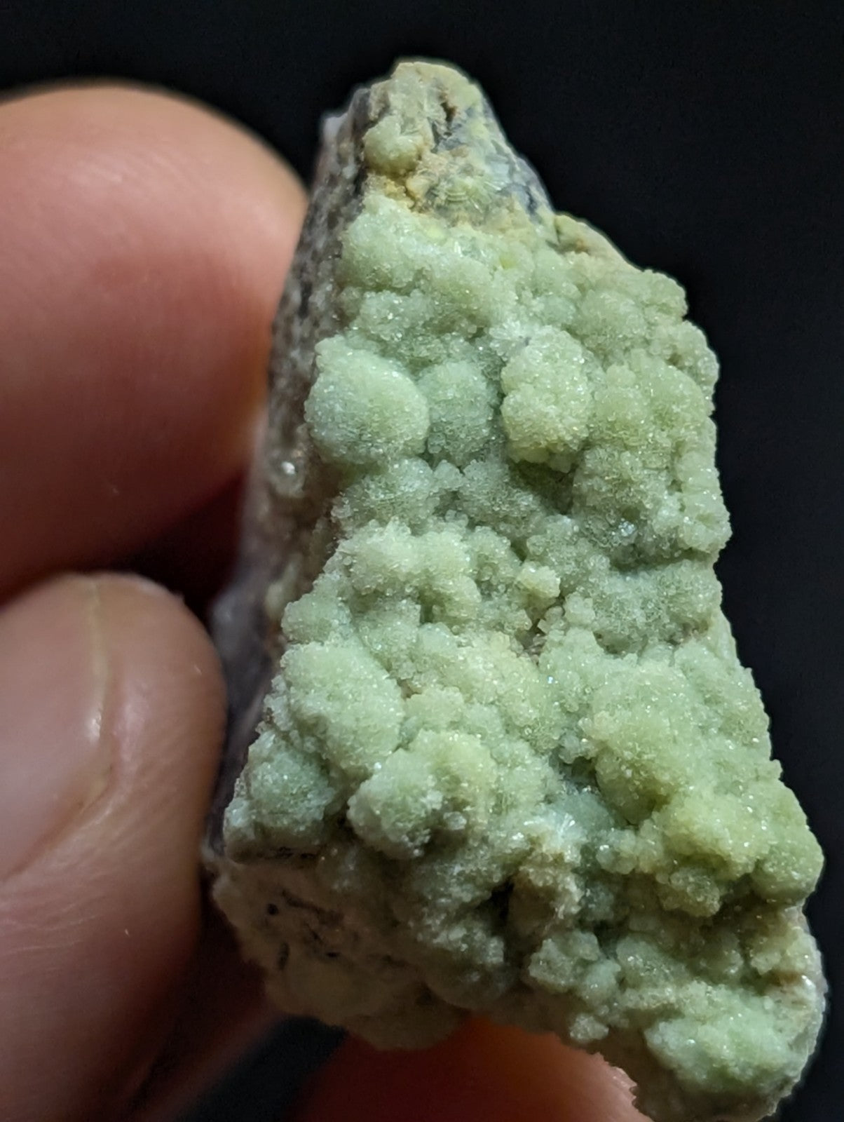A pale green, crystalline mineral specimen with a rough, textured surface and small, rounded growths.