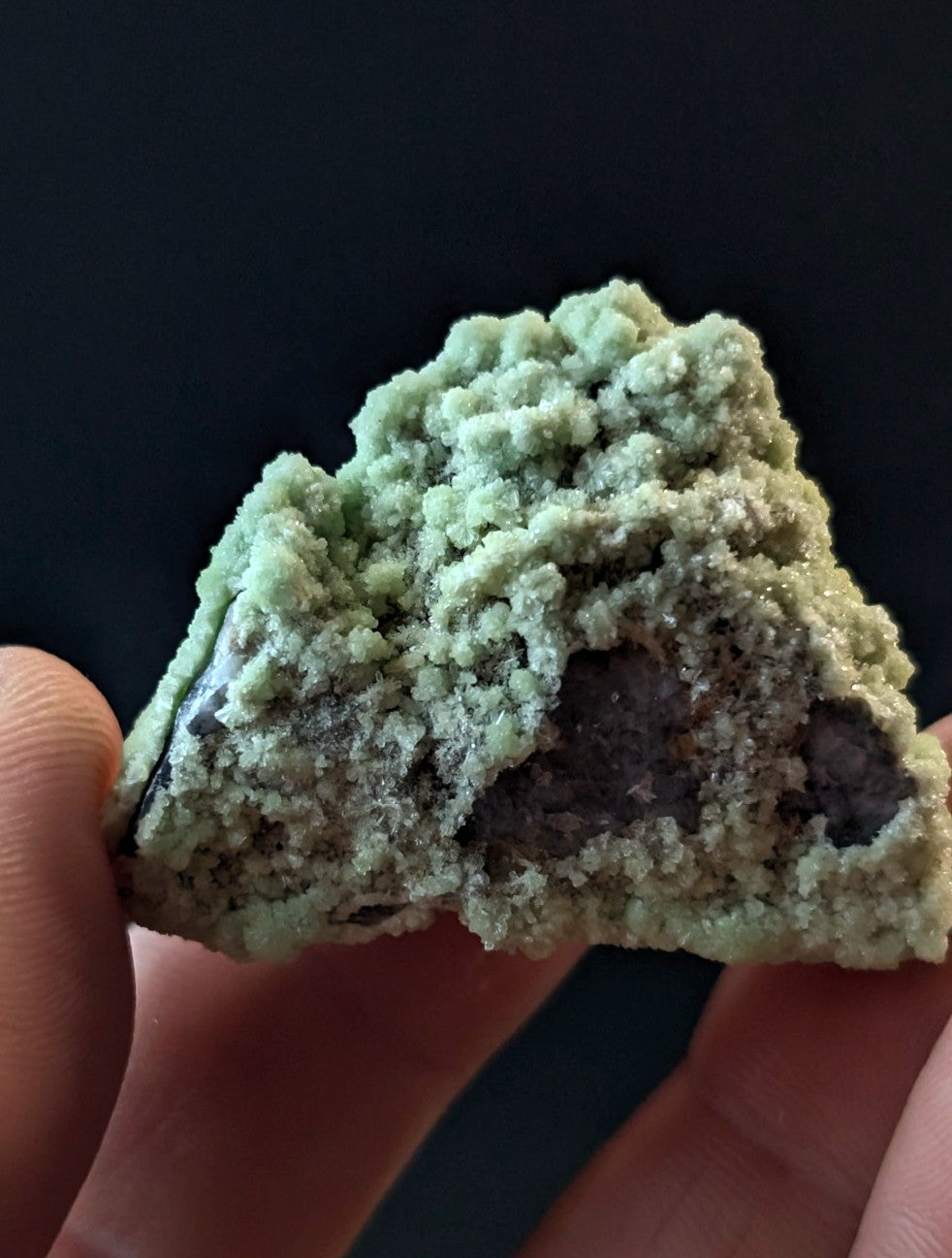A textured, light green mineral specimen with a crystalline surface and darker interior.