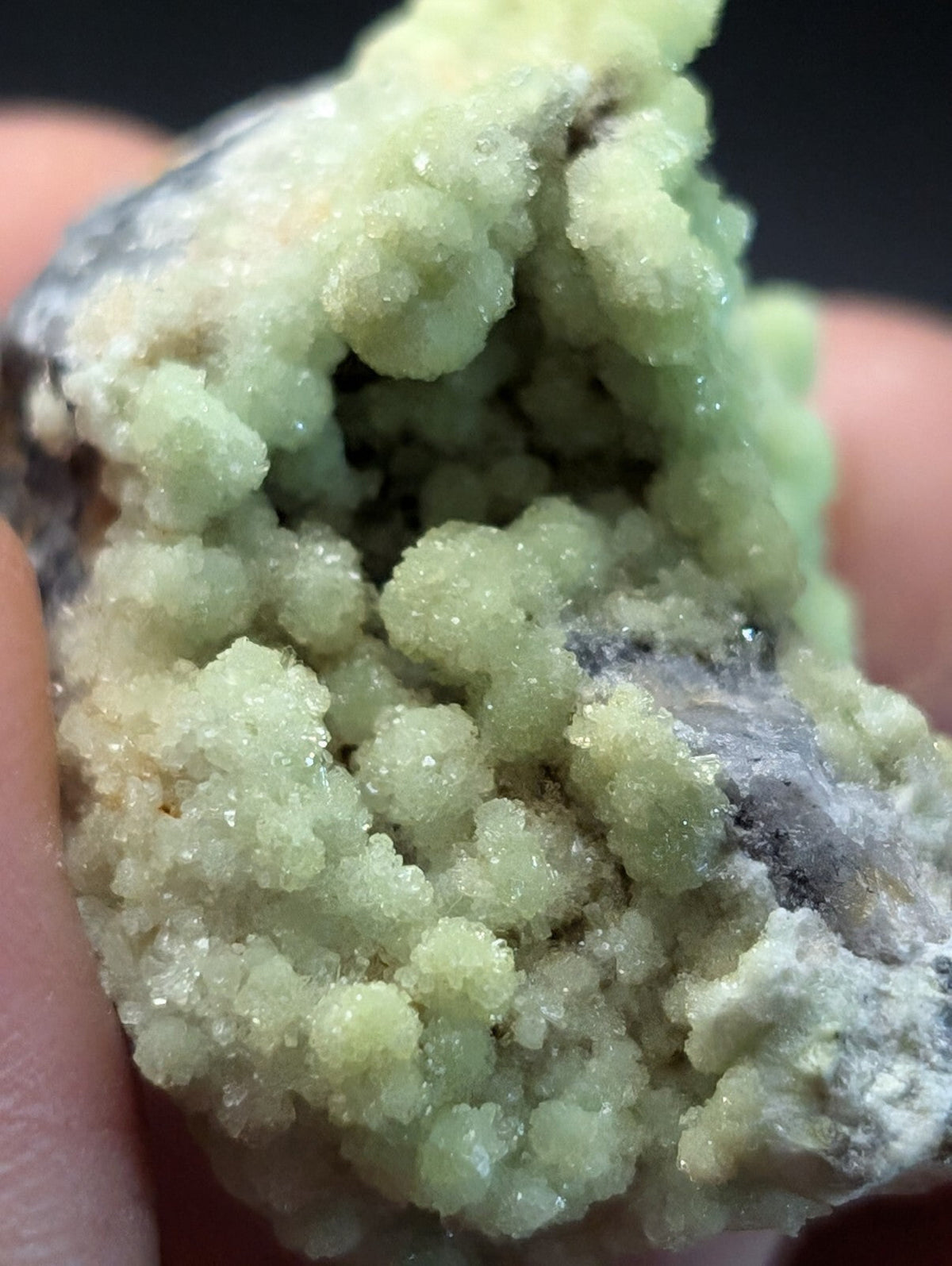 A cluster of translucent, pale green crystals with a crystalline texture and some darker grayish matrix material.