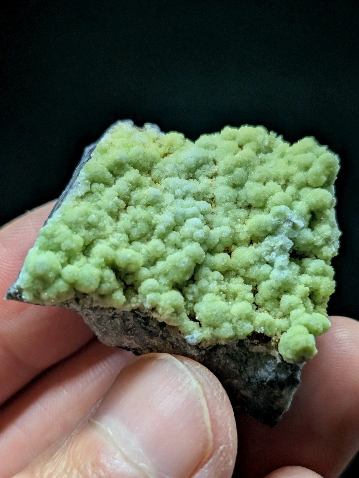 A vibrant green, bumpy mineral specimen with a textured surface held in hand.