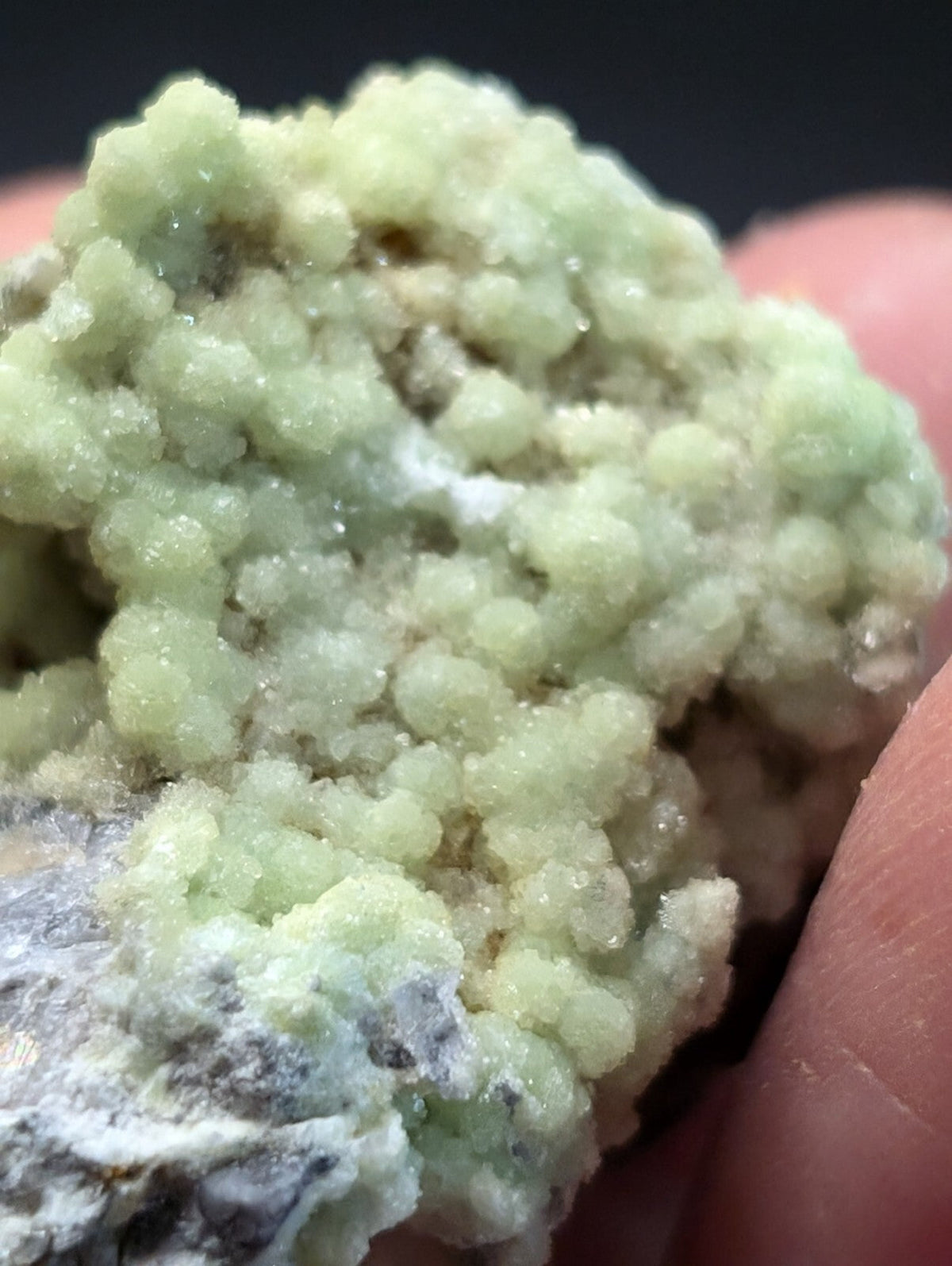 A cluster of pale green, crystalline minerals with a textured, bumpy surface and some white mineral veins.