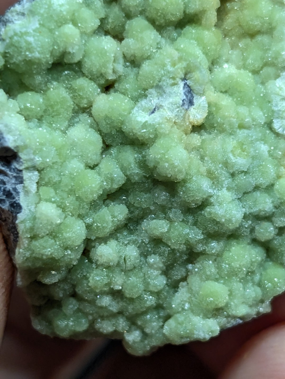 A cluster of vibrant, translucent green crystals with a rough, bumpy texture and some white crystalline patches.