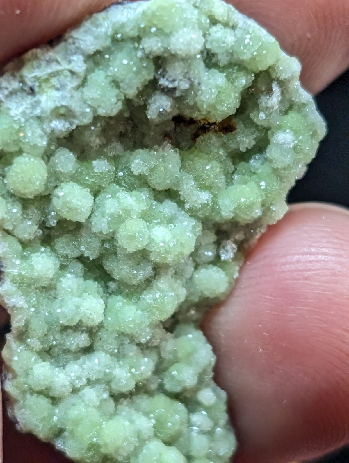 A pale green, crystalline mineral specimen with a textured, bumpy surface held between fingers.