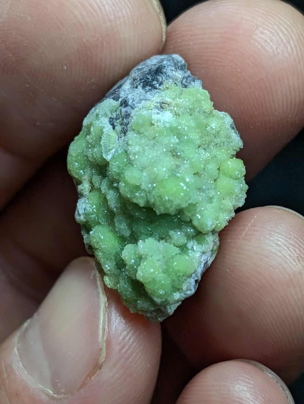 A vibrant green, crystalline mineral specimen with a rough, textured surface and patches of grayish matrix.