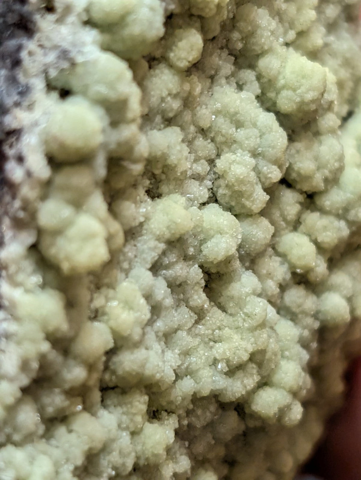 A cluster of pale green, crystalline mineral formations with a rough, textured surface.