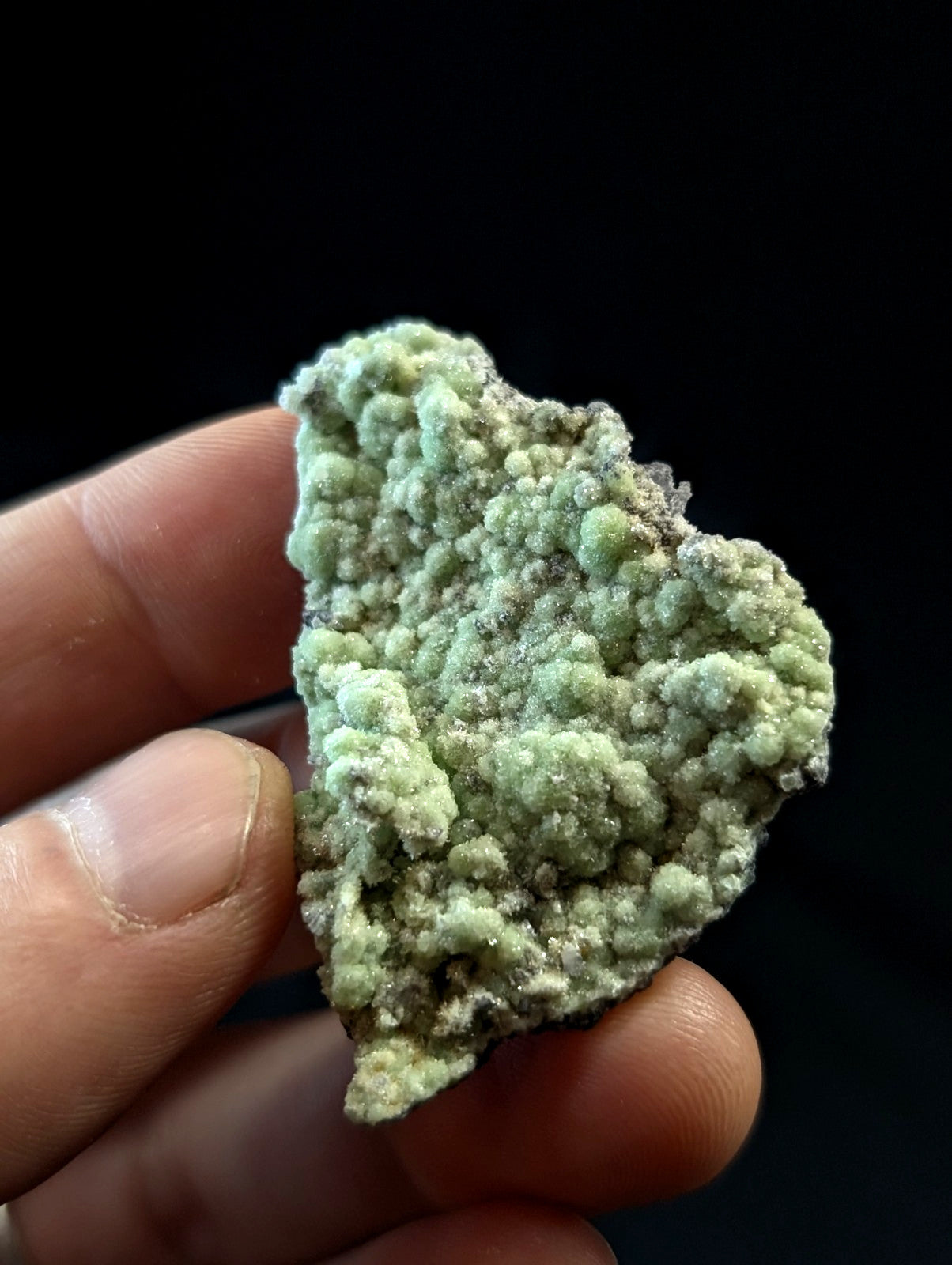 A textured, light green mineral specimen with a rough, bumpy surface held between fingers.