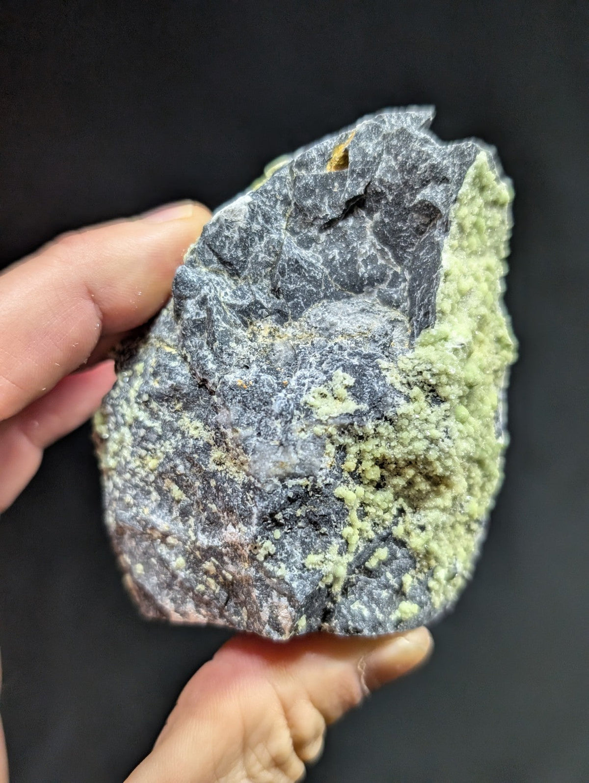 A rough, irregularly shaped mineral specimen with a dark gray base and patches of vibrant green crystalline growths.