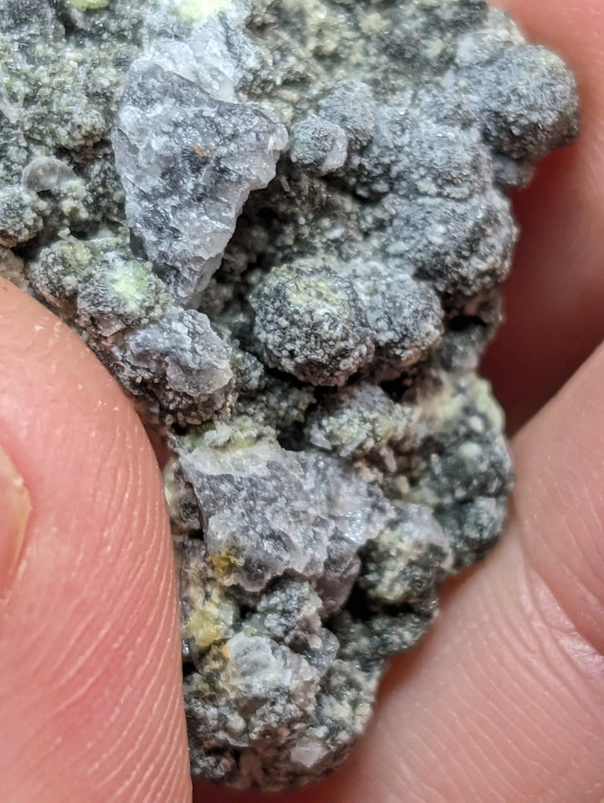 A rough, grayish-green mineral specimen with a textured surface and translucent crystalline formations.