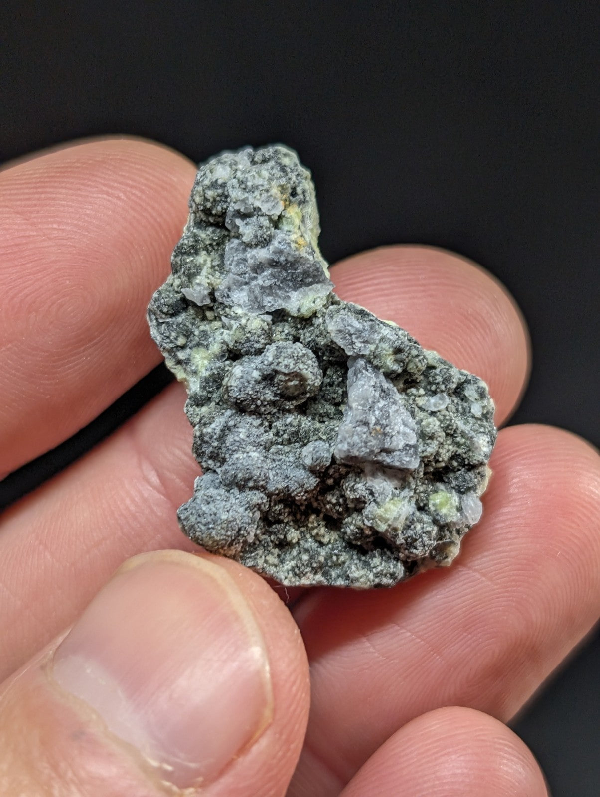 A rough, irregularly shaped mineral specimen with a mottled green and gray surface texture.