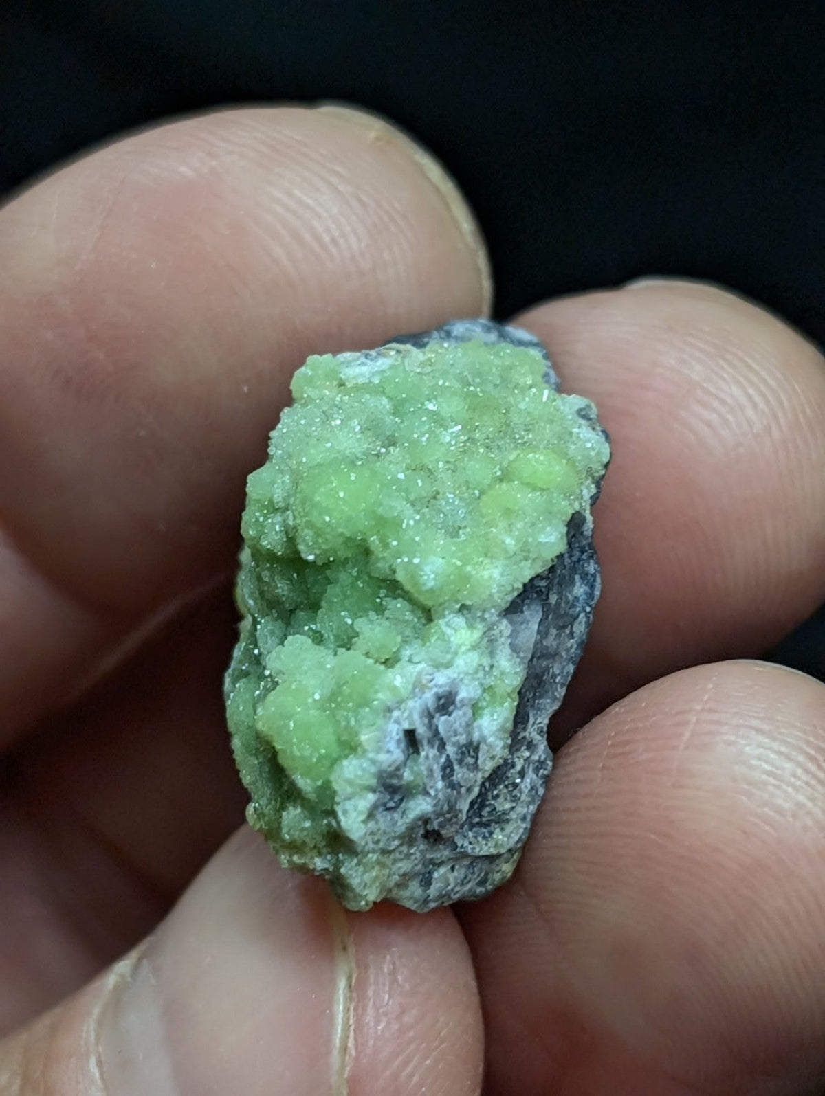 A vibrant green, crystalline mineral specimen with a rough, textured surface and embedded gray rock matrix.