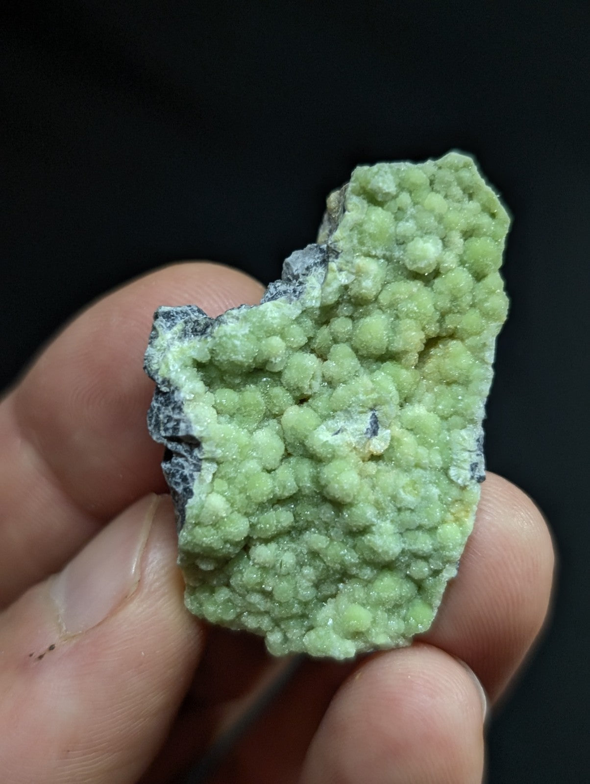 A vibrant green, bumpy mineral specimen with a rough, textured surface and speckles of darker gray.