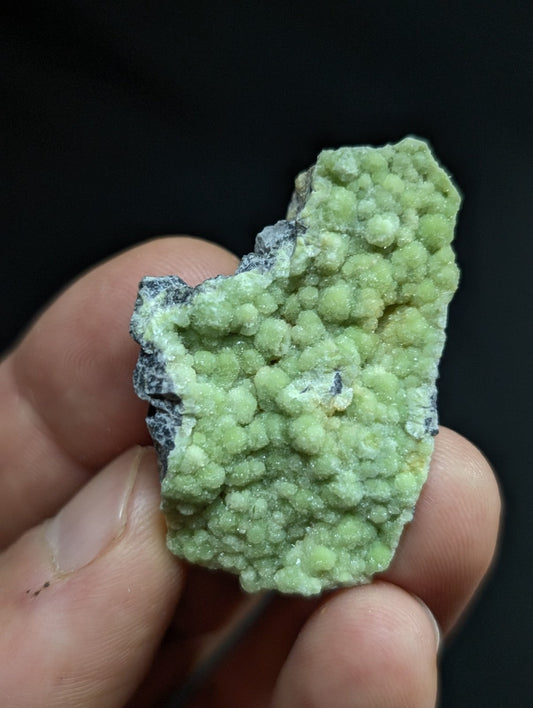 A vibrant green, bumpy mineral specimen with a rough, textured surface and speckles of darker gray.