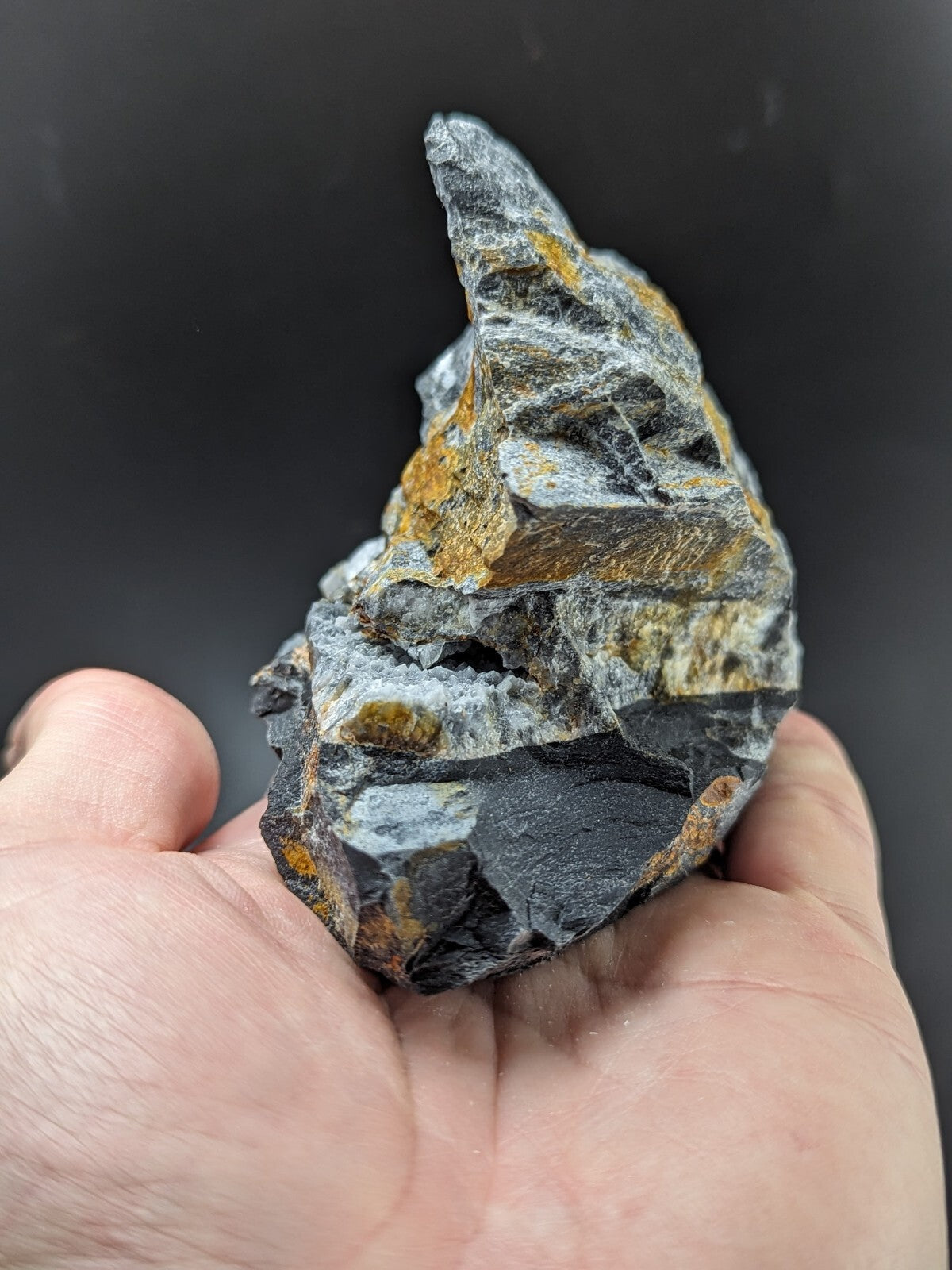 A rugged, irregularly shaped mineral specimen with a dark gray base and patches of vibrant golden-yellow streaks.