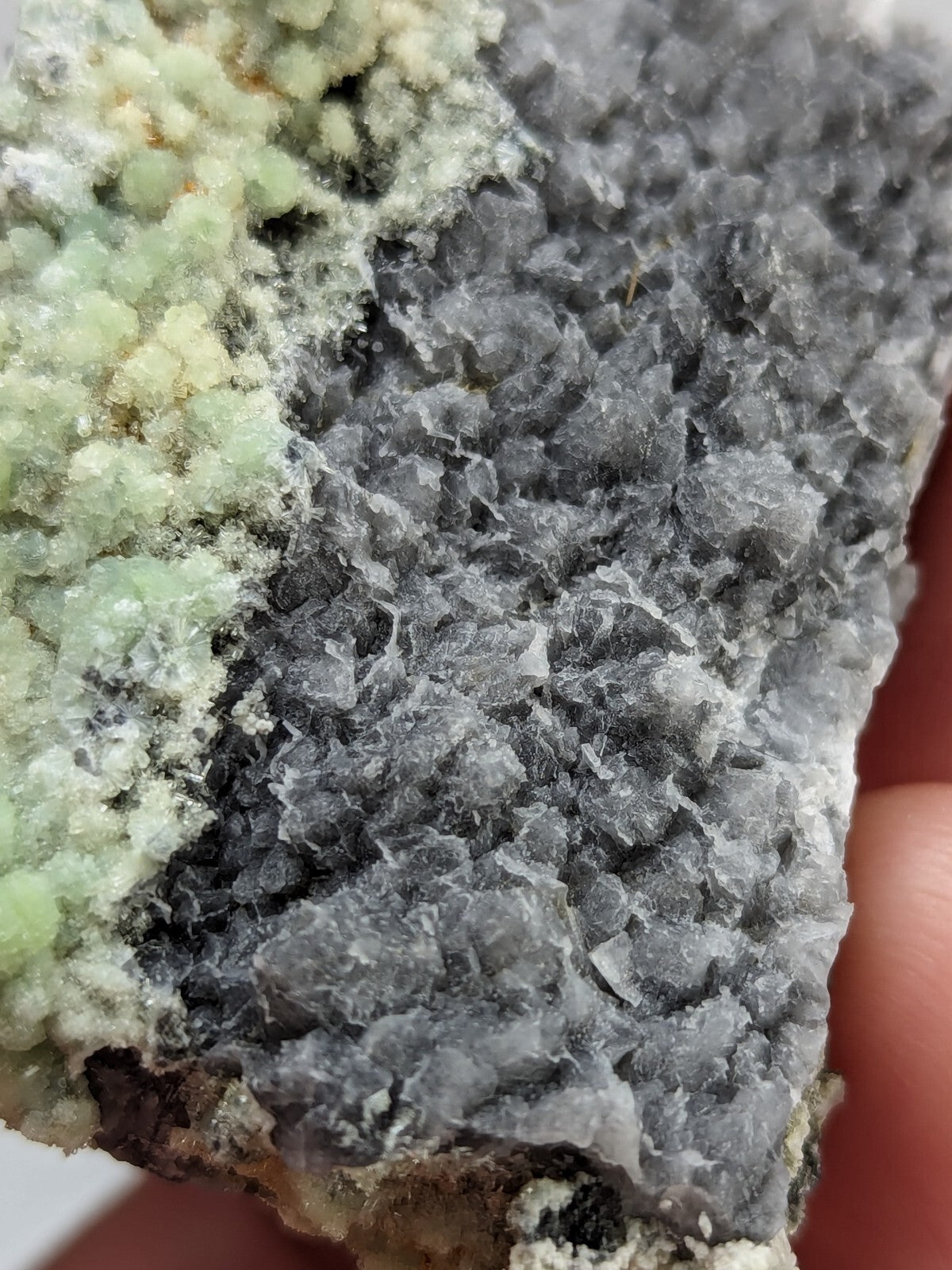 A textured mineral specimen featuring a gray crystalline matrix with patches of pale green, possibly showcasing a natural geological formation.