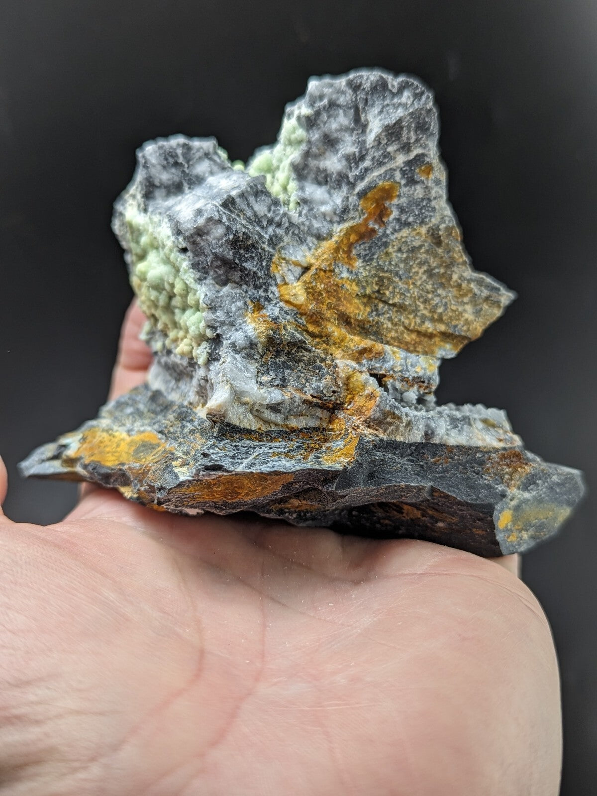 A rugged, naturally occurring mineral specimen featuring a striking combination of dark gray rock with patches of vibrant yellow and pale green crystalline formations.