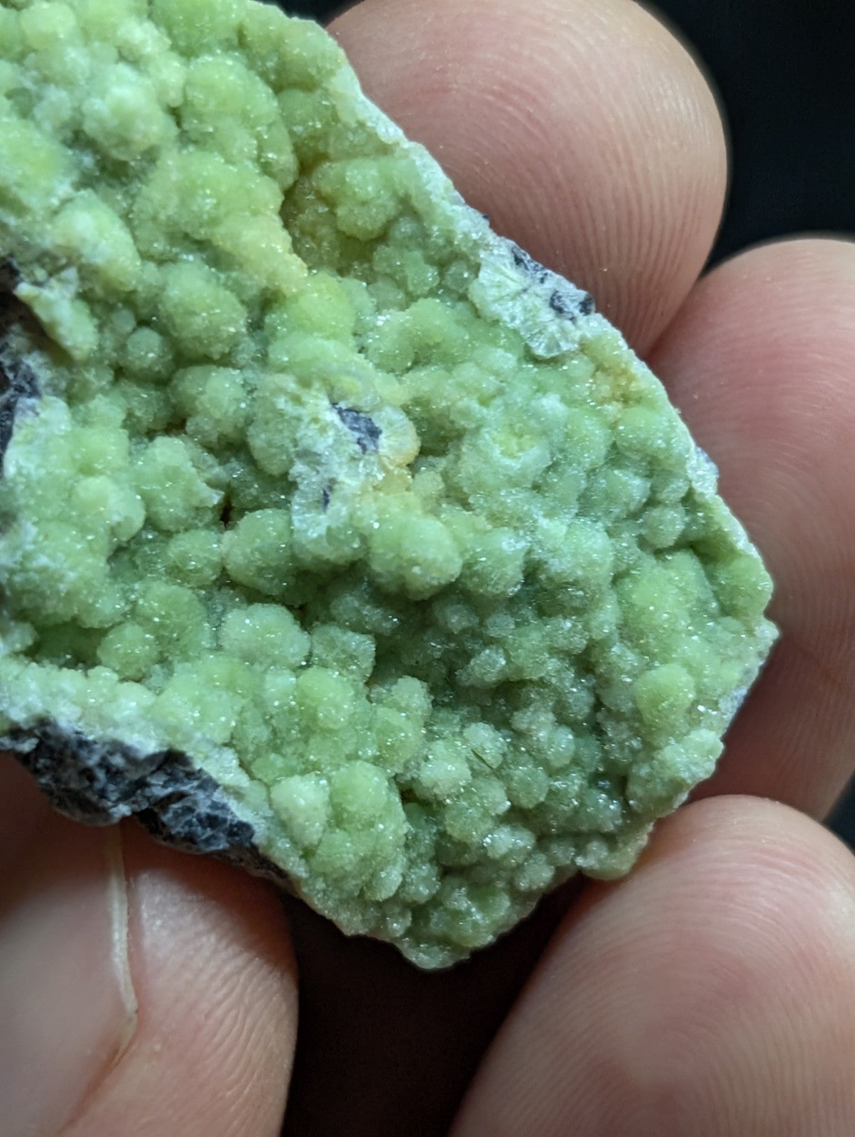 A hand holds a light green, crystalline mineral specimen with rounded, bubbly formations and a rough, natural surface.