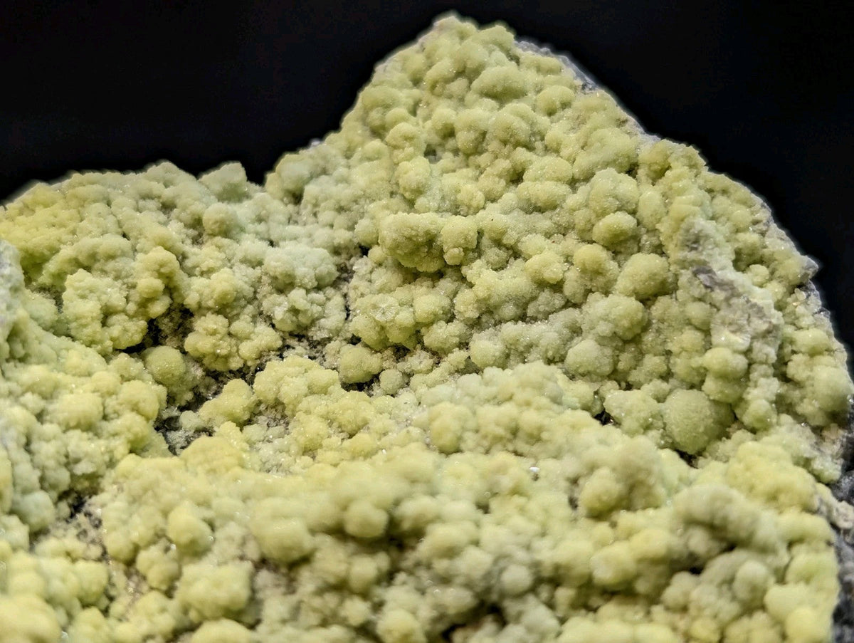 A cluster of pale yellow, bumpy mineral crystals with a rough, textured surface.