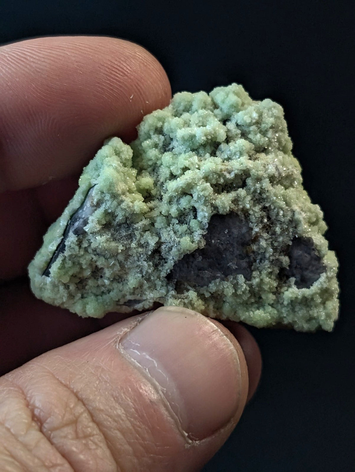 A textured, light green mineral specimen with a crystalline surface and dark gray core.