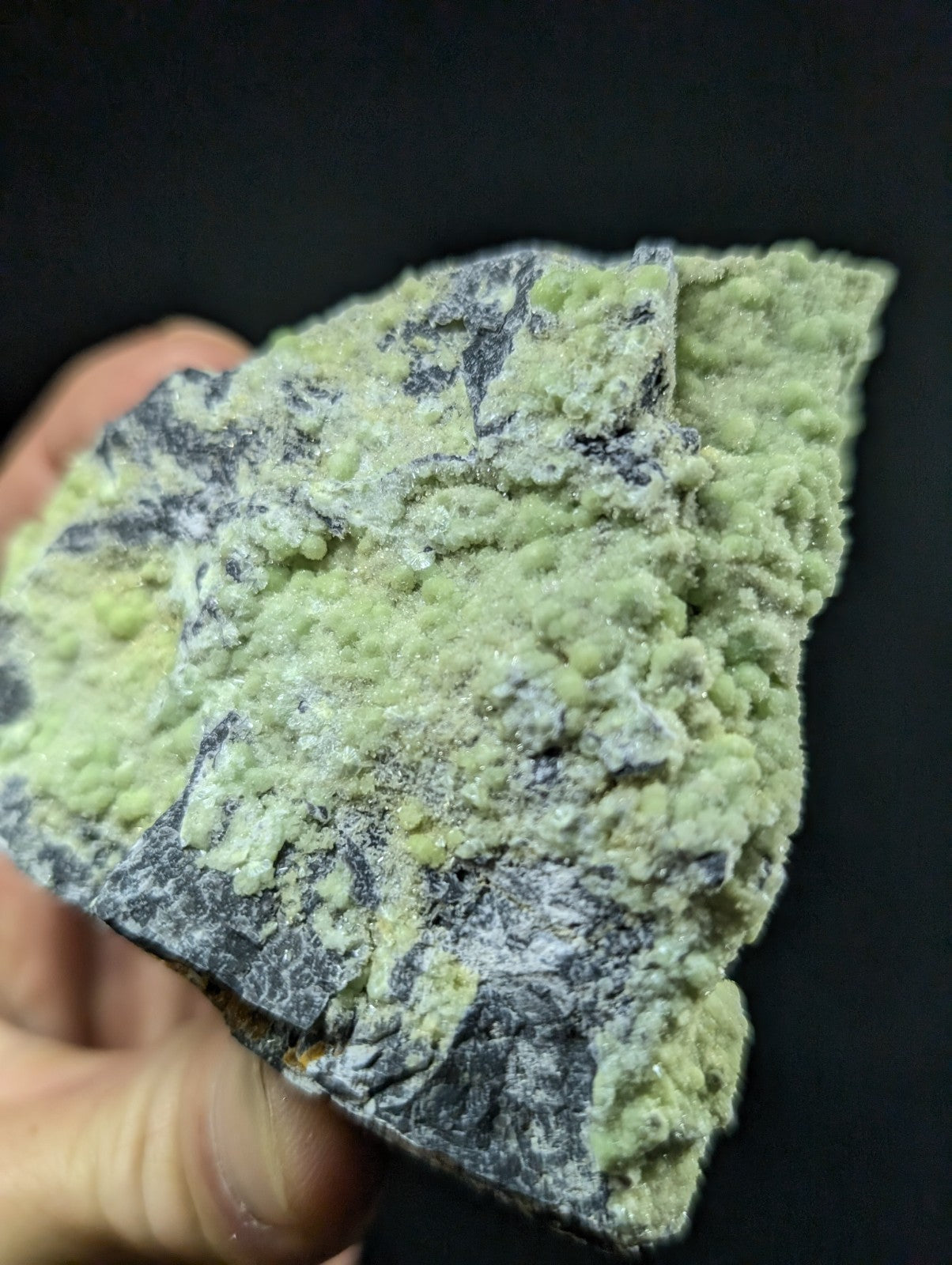A rough, irregularly shaped mineral specimen with a textured surface featuring patches of pale green and dark gray.