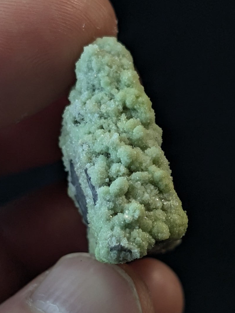 A pale green, crystalline mineral specimen with a rough, textured surface held between fingers.