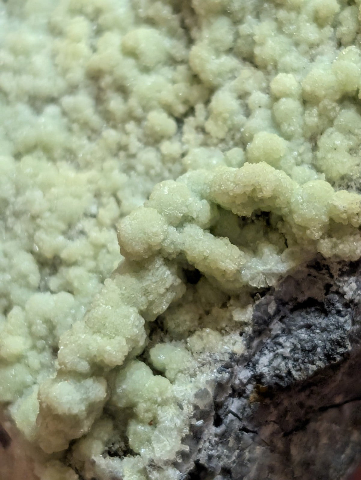 A cluster of pale green, crystalline mineral formations with a rough, textured surface.