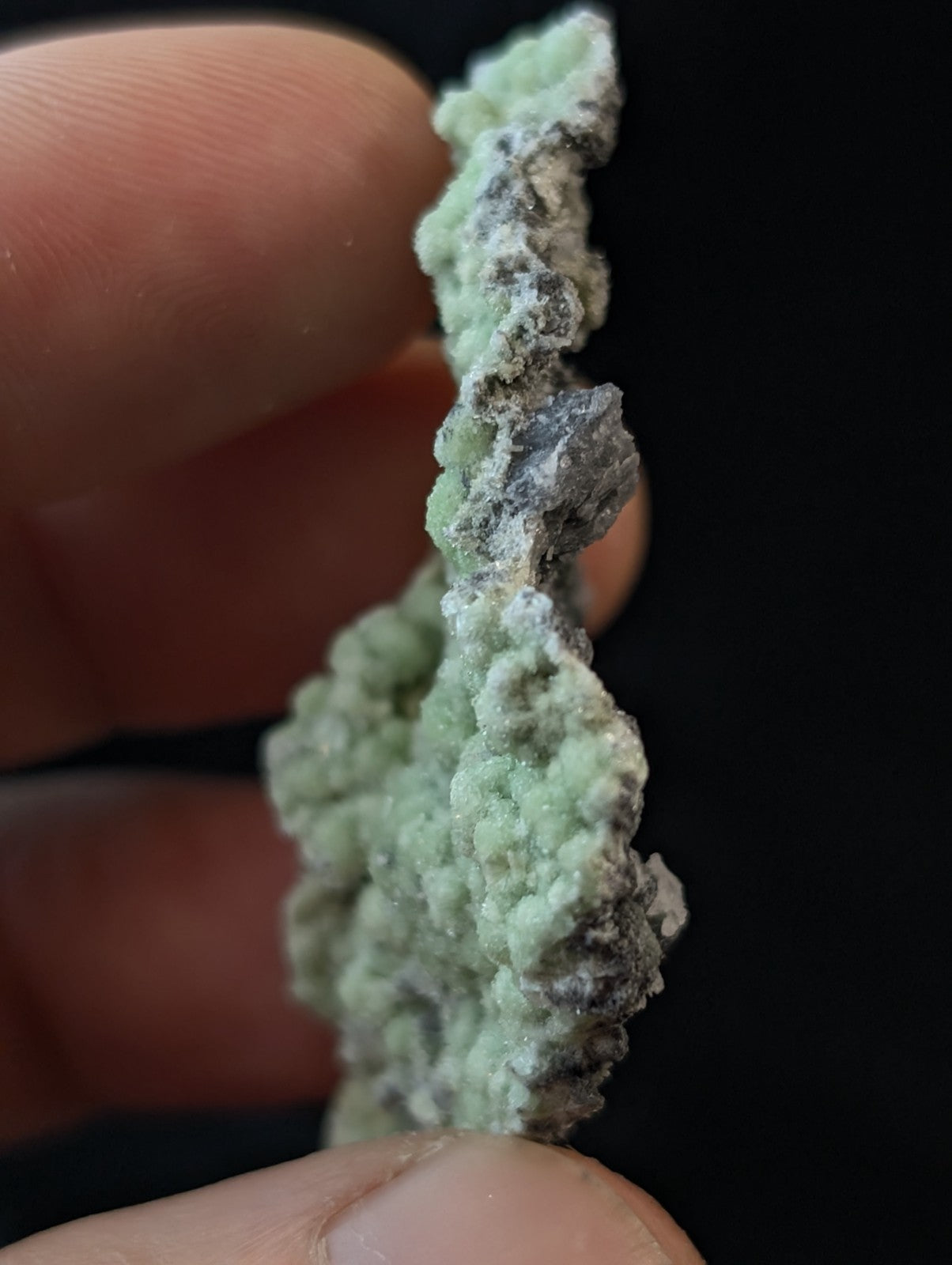 A delicate, light green mineral specimen with a textured, crystalline surface and subtle grayish patches.