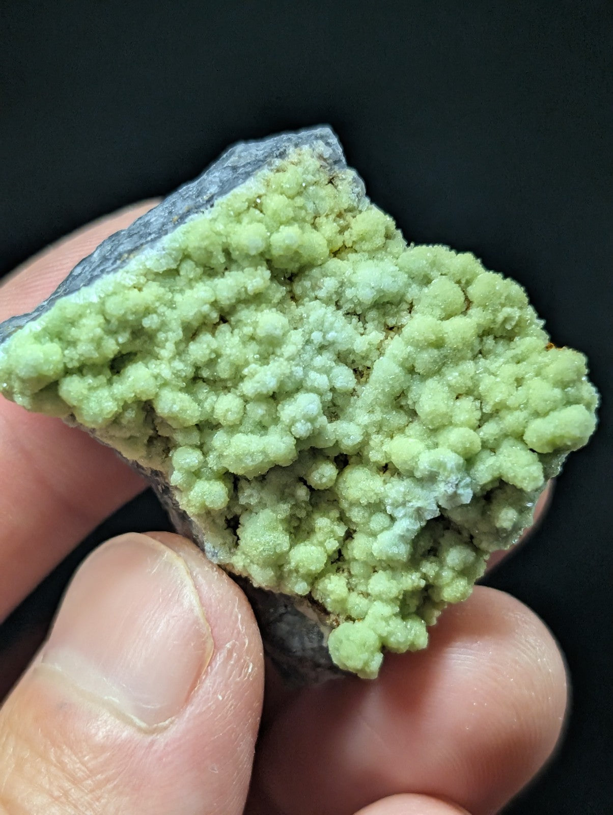 A vibrant green, bubbly mineral specimen with a rough, textured surface and grayish rock base.
