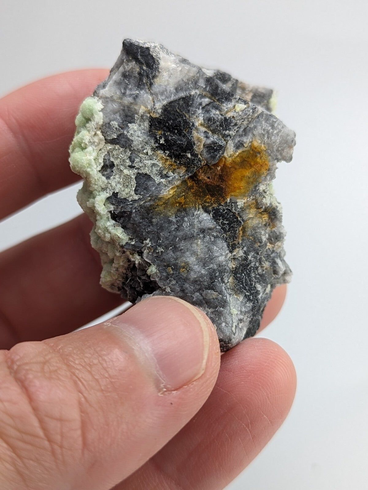 A rugged, irregularly shaped mineral specimen with a mottled gray surface accented by patches of vibrant yellow and soft green.