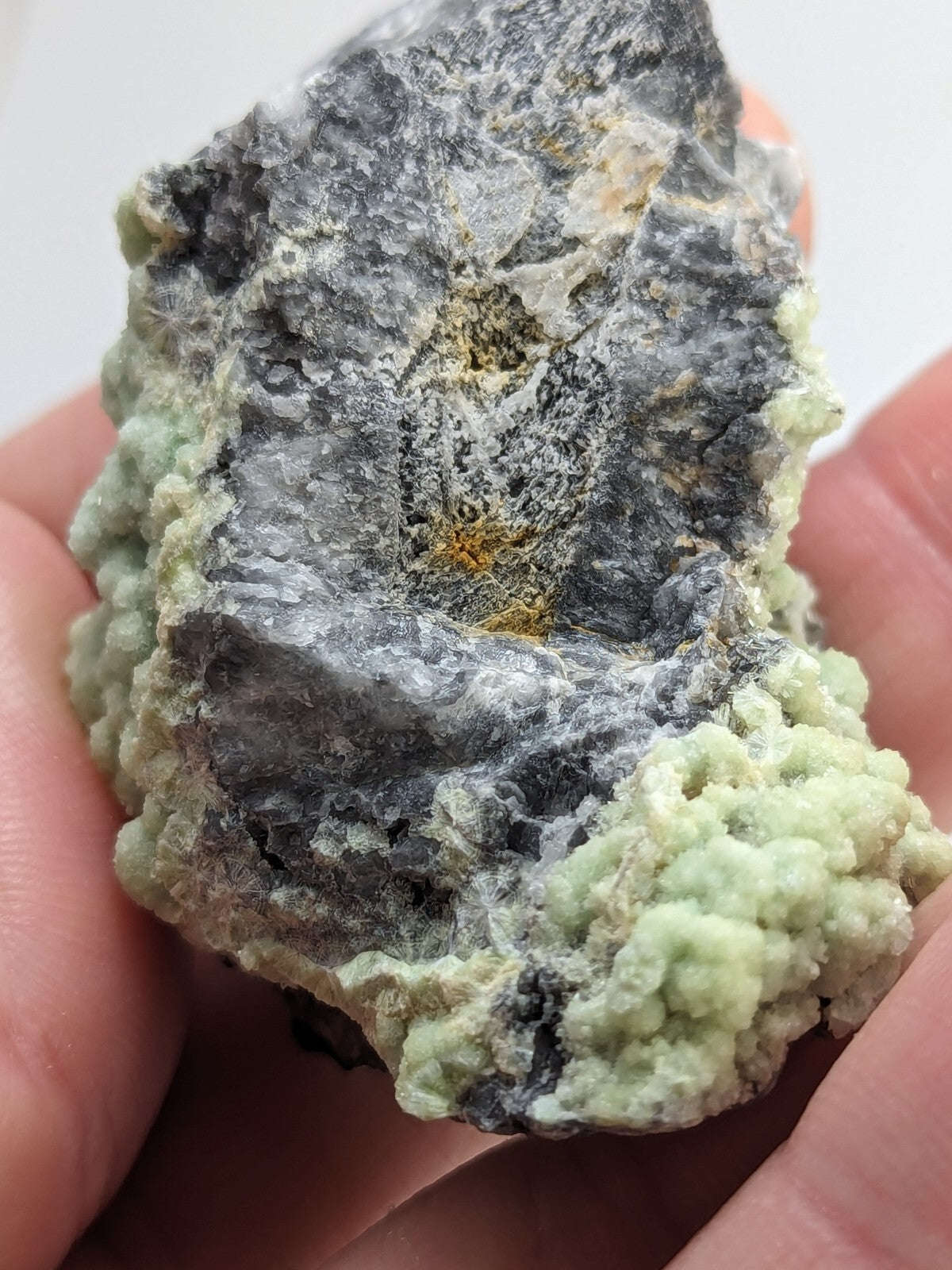 A rough, irregularly shaped mineral specimen featuring a dark gray base with patches of pale green and subtle golden-yellow inclusions.