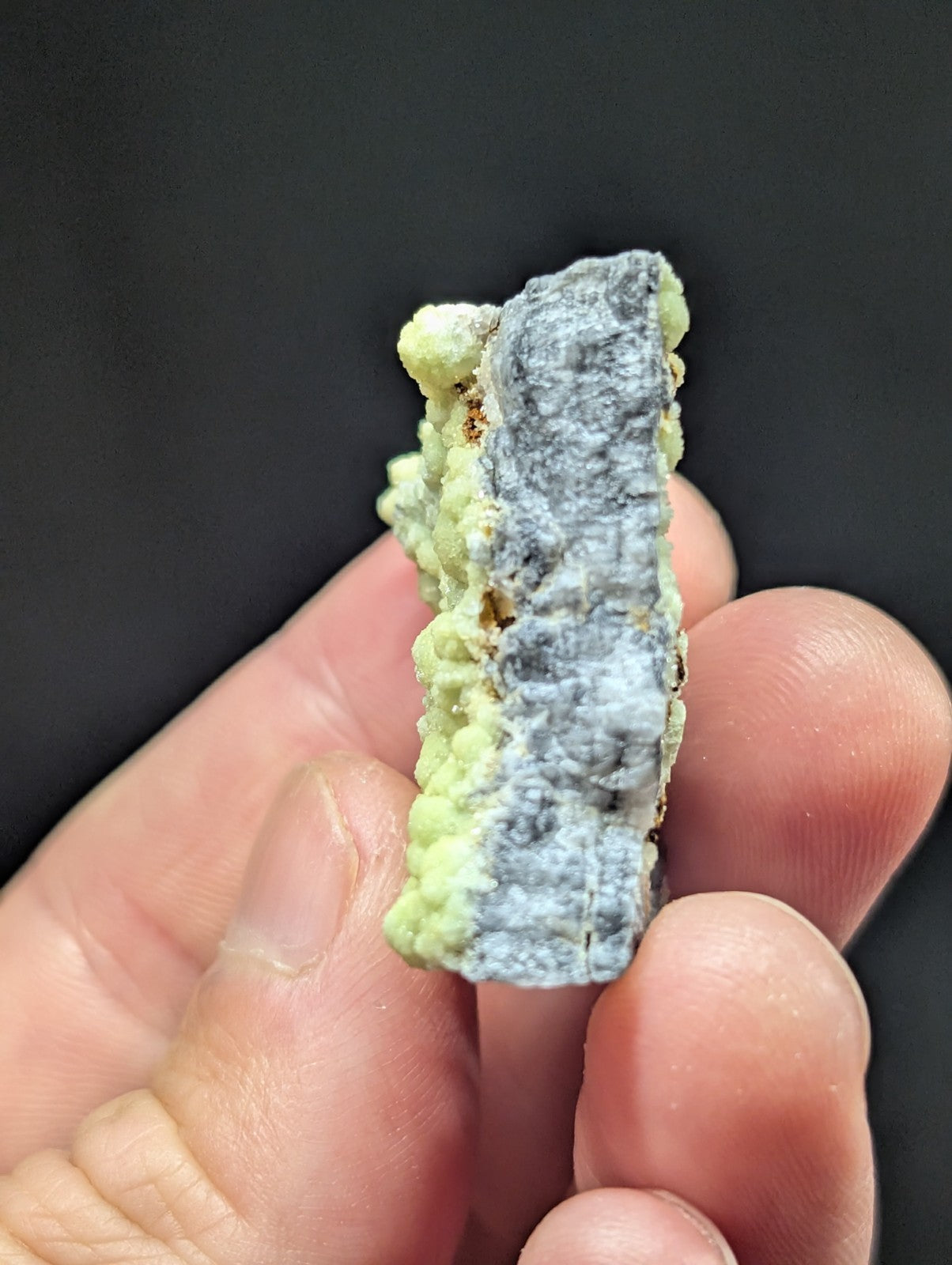 A textured mineral specimen with a grayish central section and light green, crystalline growths on its sides.