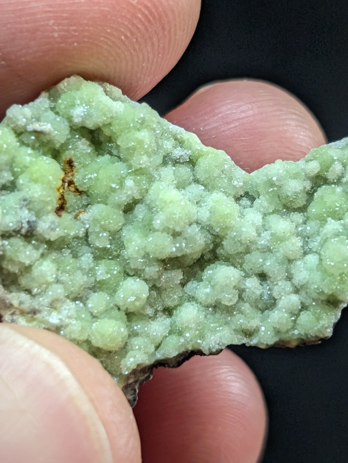 A pale green, crystalline mineral specimen with a textured surface of rounded, bubble-like formations.