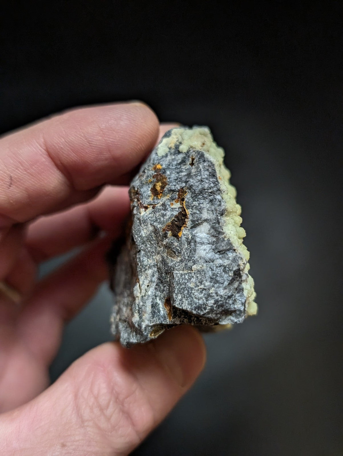 A rough, irregularly shaped mineral specimen with a grayish base and patches of yellow-green crystalline growths.