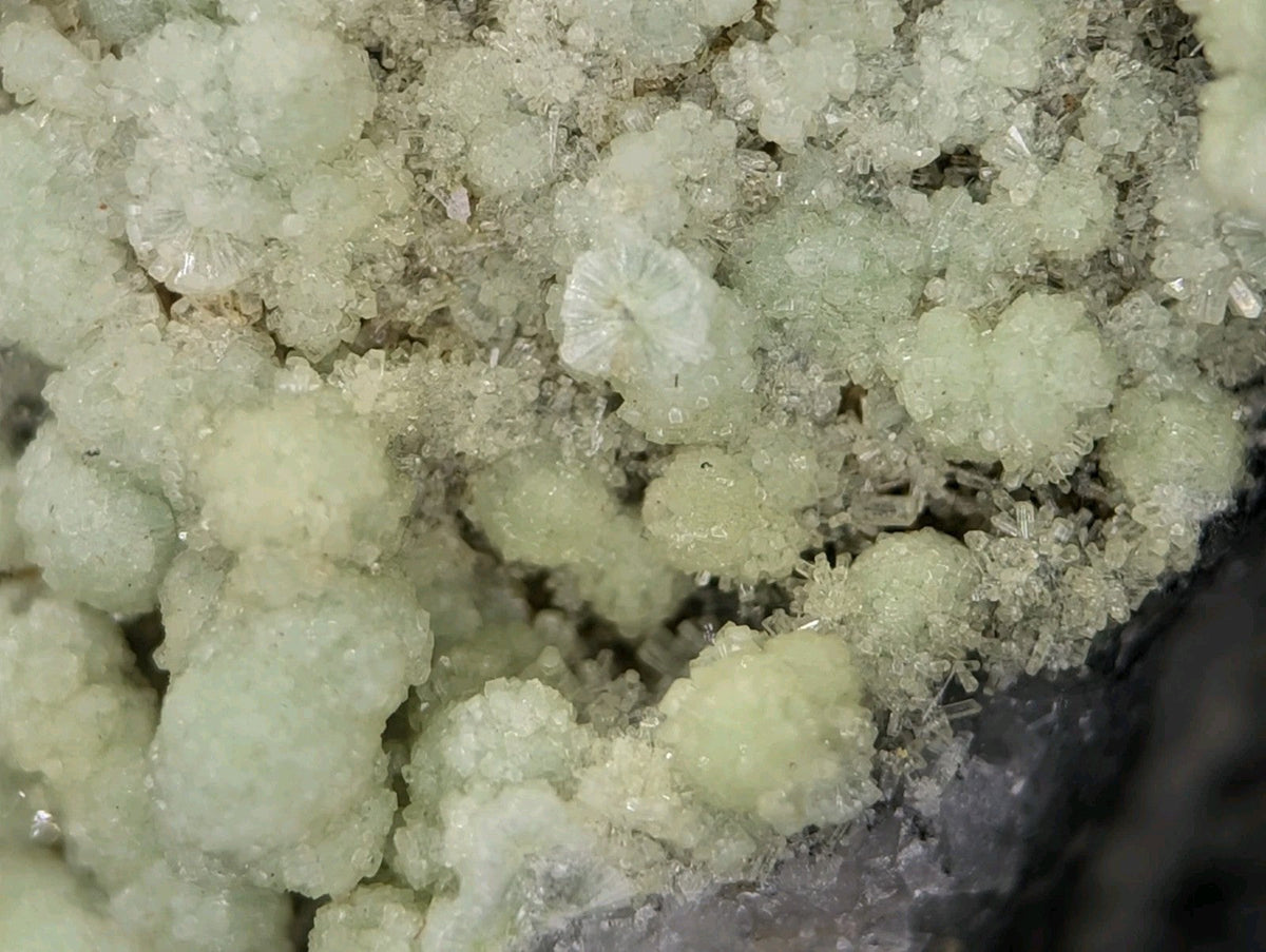 A cluster of translucent, pale green crystalline formations with a rough, textured surface.