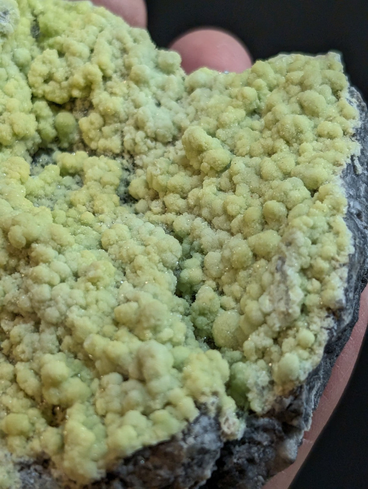 A vibrant, pale green mineral specimen with a textured, clustered surface held in hand.