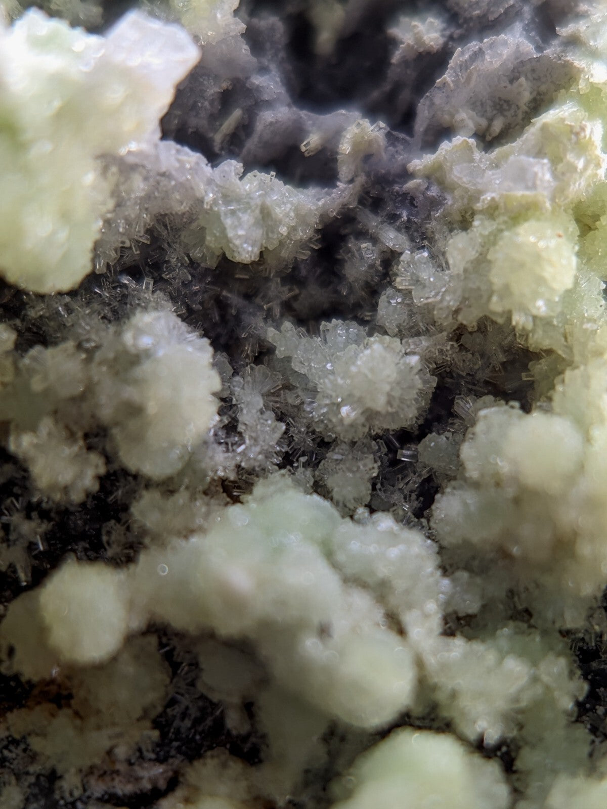 Pale green crystalline mineral formations with translucent, faceted structures clustered against a darker, earthy matrix.