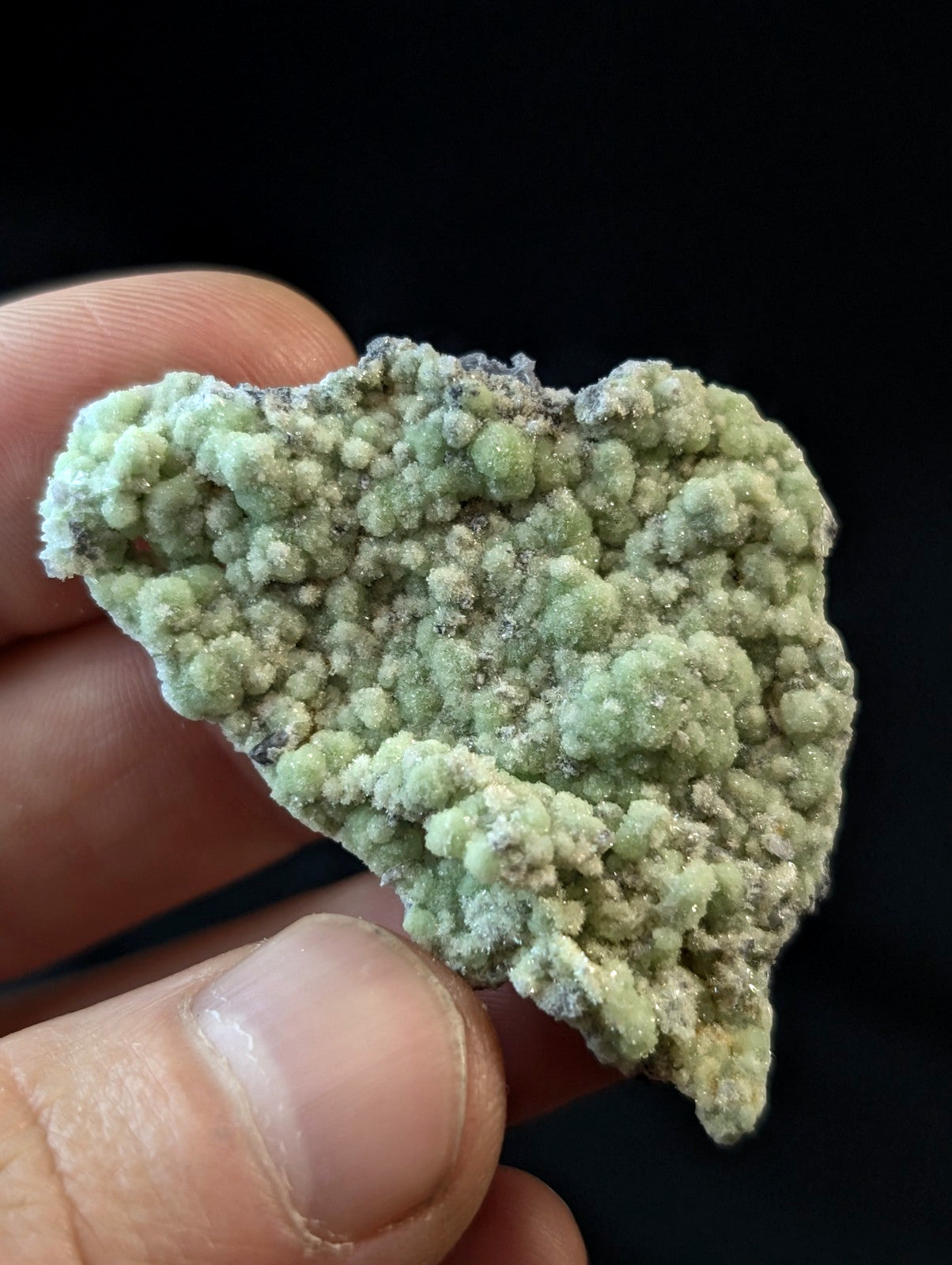 A textured, light green mineral specimen with a bumpy, crystalline surface held between fingers.