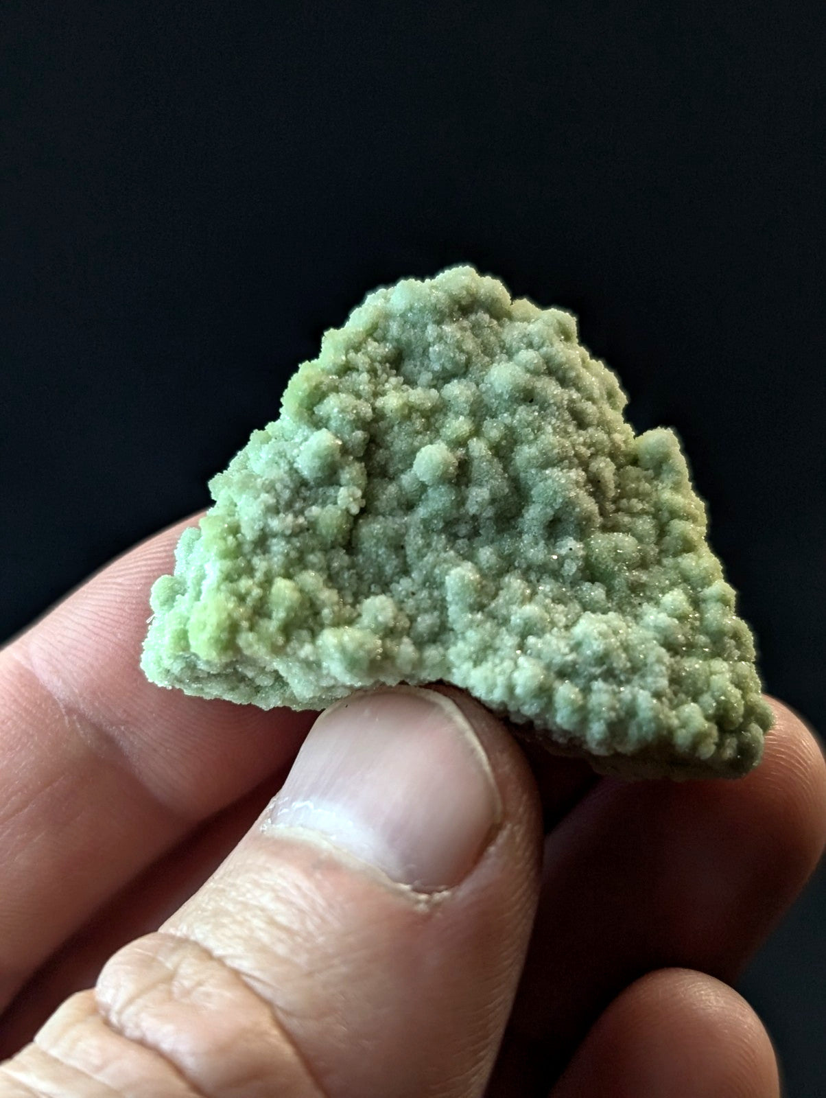 A textured, light green mineral specimen with a rough, bumpy surface held between fingers.