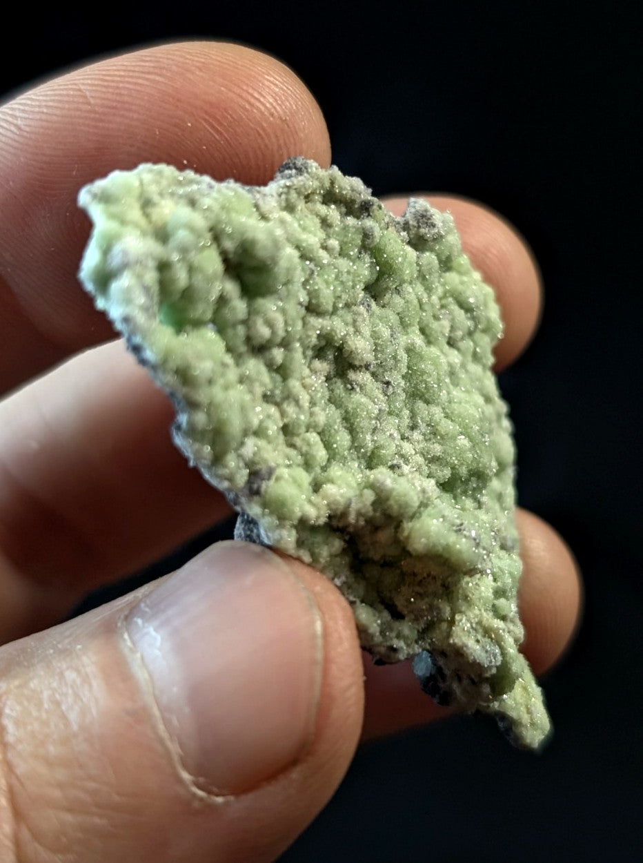 A textured, light green mineral specimen with a rough, crystalline surface and subtle darker patches.